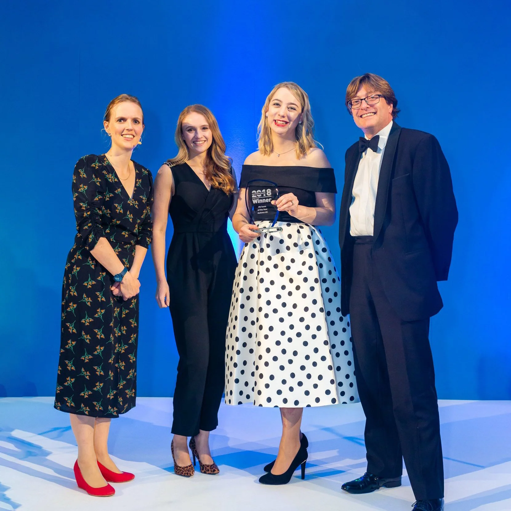 Cat and her team in formal attire standing on a stage, holding an award plaque that reads 'Winner'