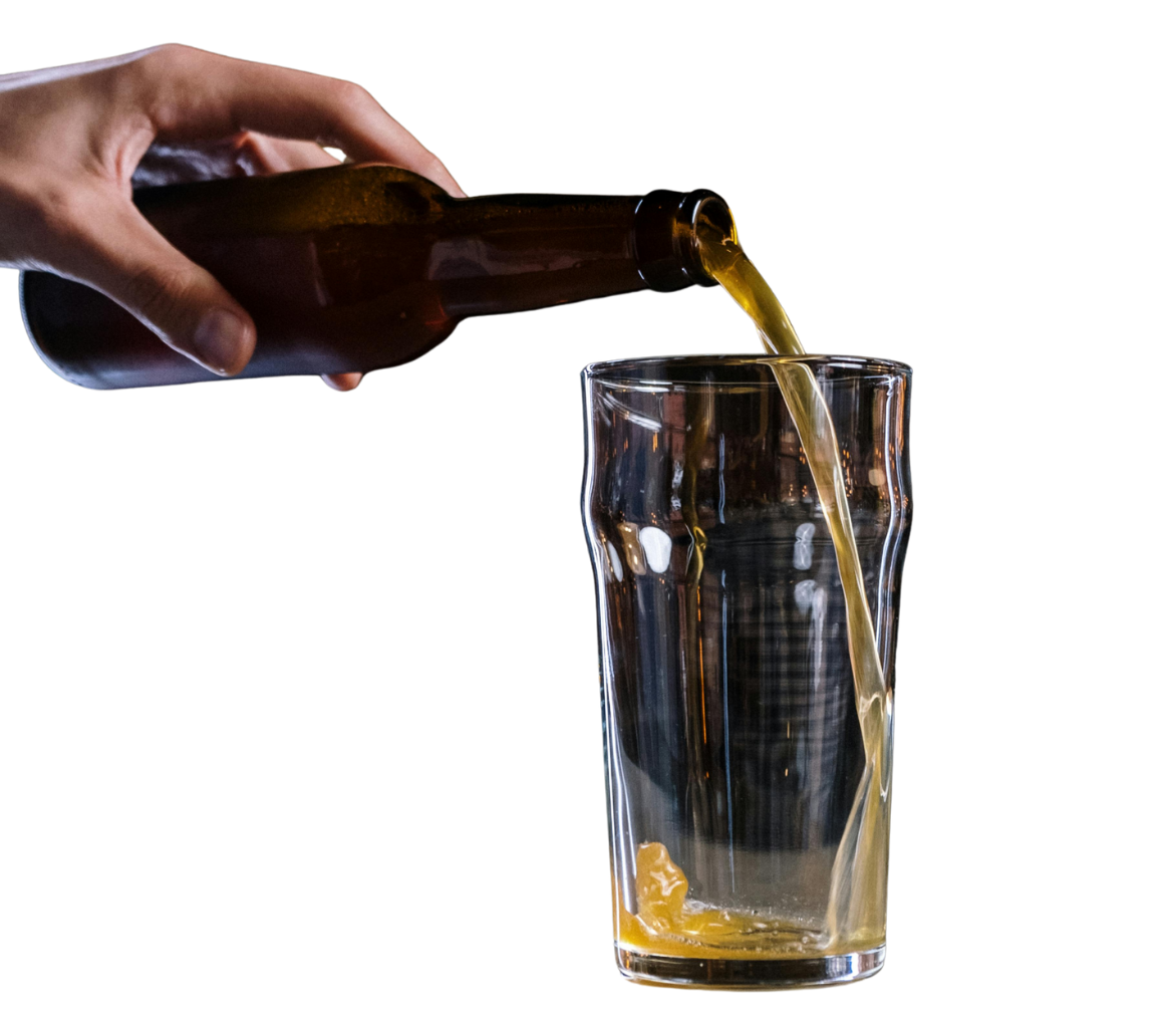 A hand pouring a brown bottle of beer into a tall glass against a black background.