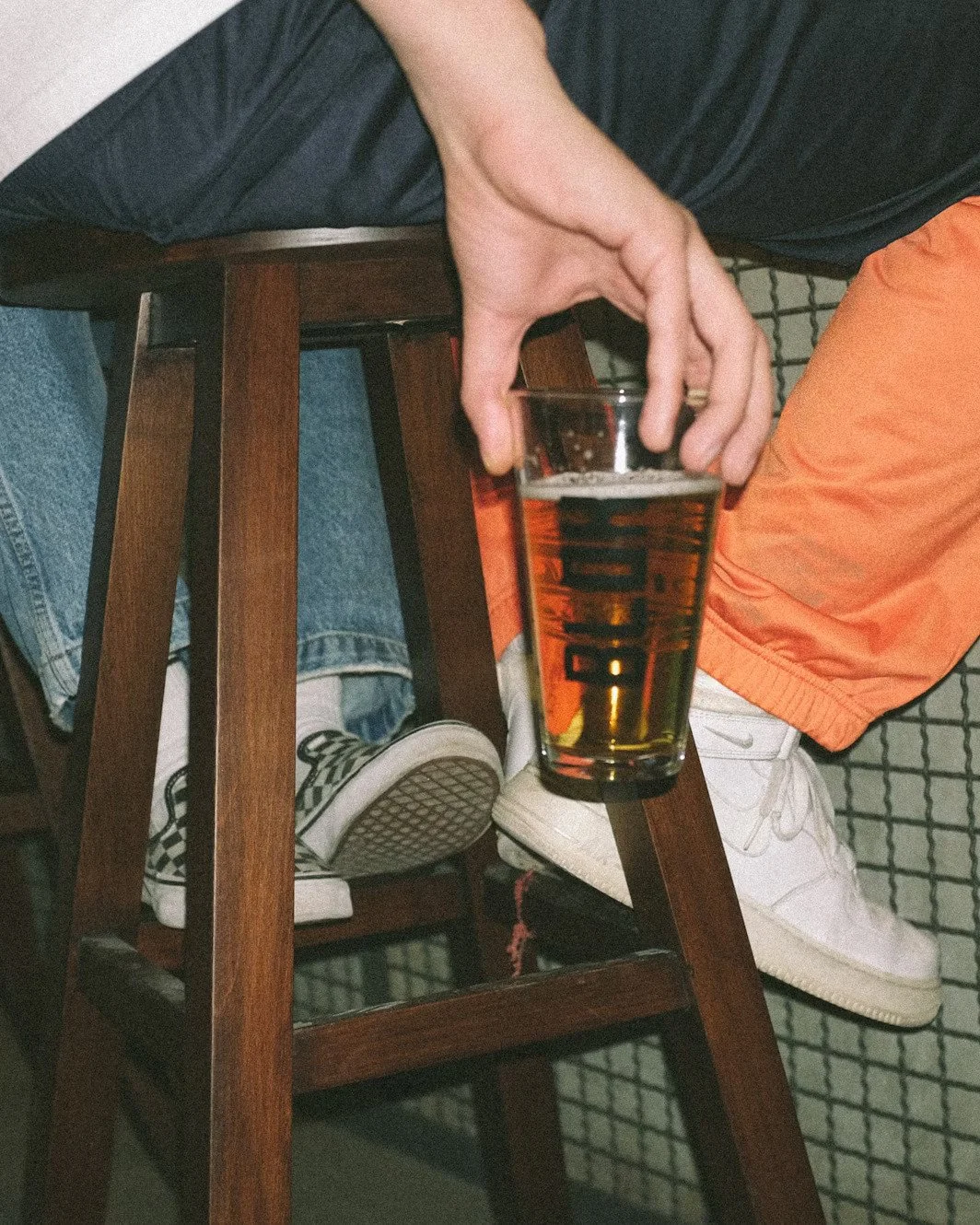 Person sitting on a chair holding a pint of beer in a glass.