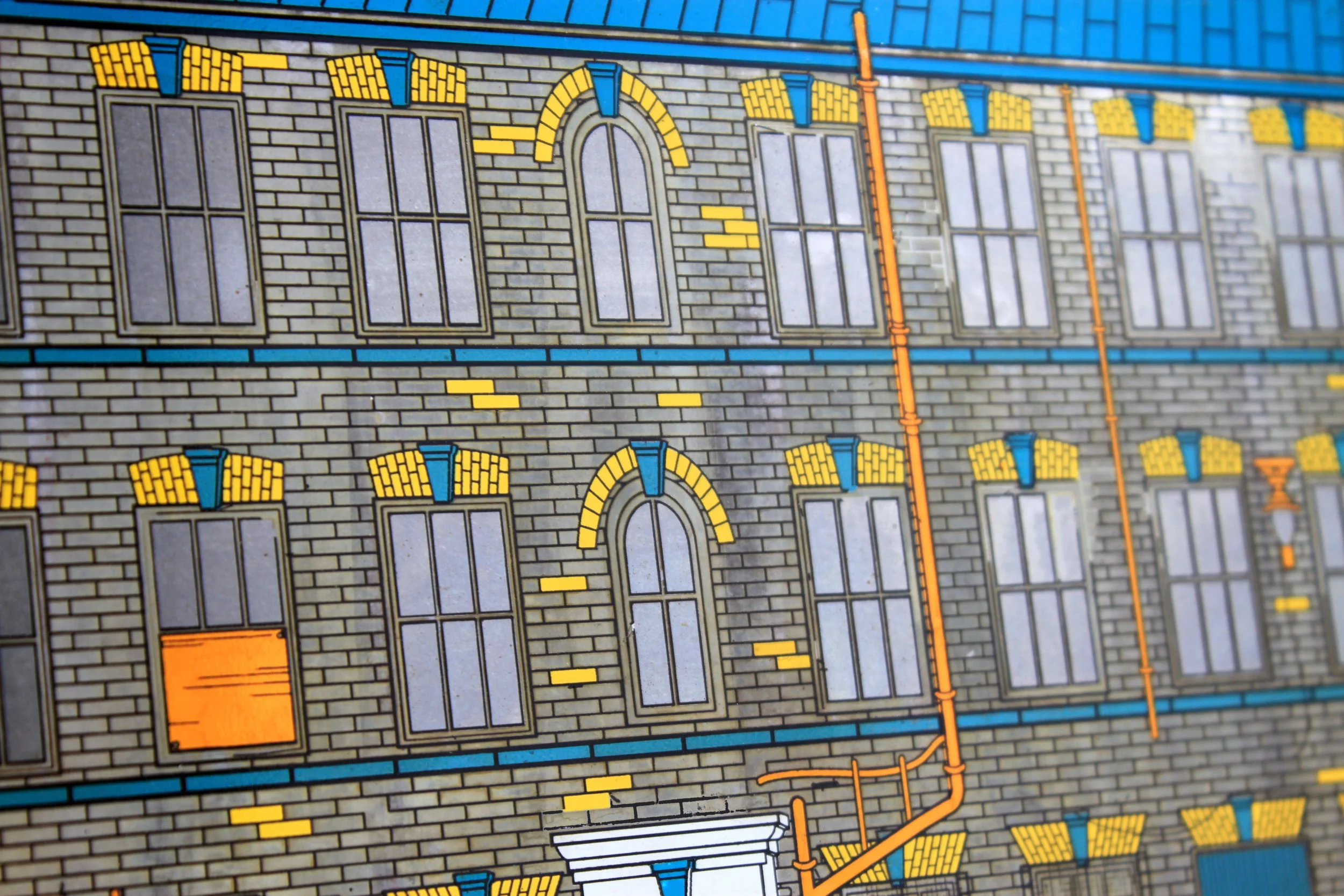 A close-up of a detailed cartoon-style illustration of a brick building facade with multiple large windows, decorative yellow brick accents, blue window trims, and orange pipes.
