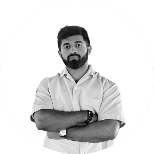 Black and white photo of a young man with crossed arms, beard, and short hair, wearing a button-up shirt, against a plain background.