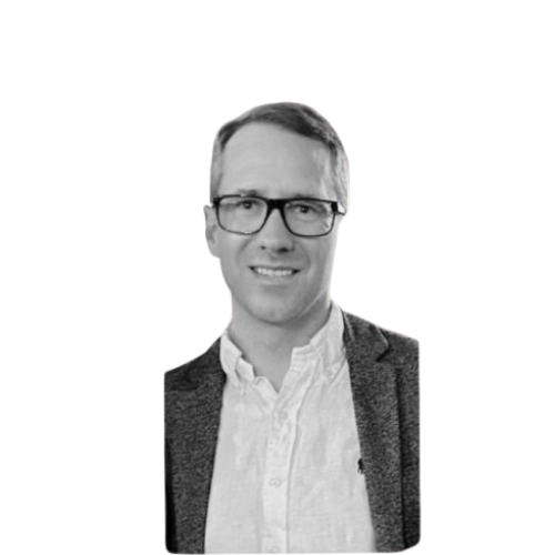 A black-and-white portrait of a man wearing glasses, a white shirt, and a gray blazer, smiling at the camera.