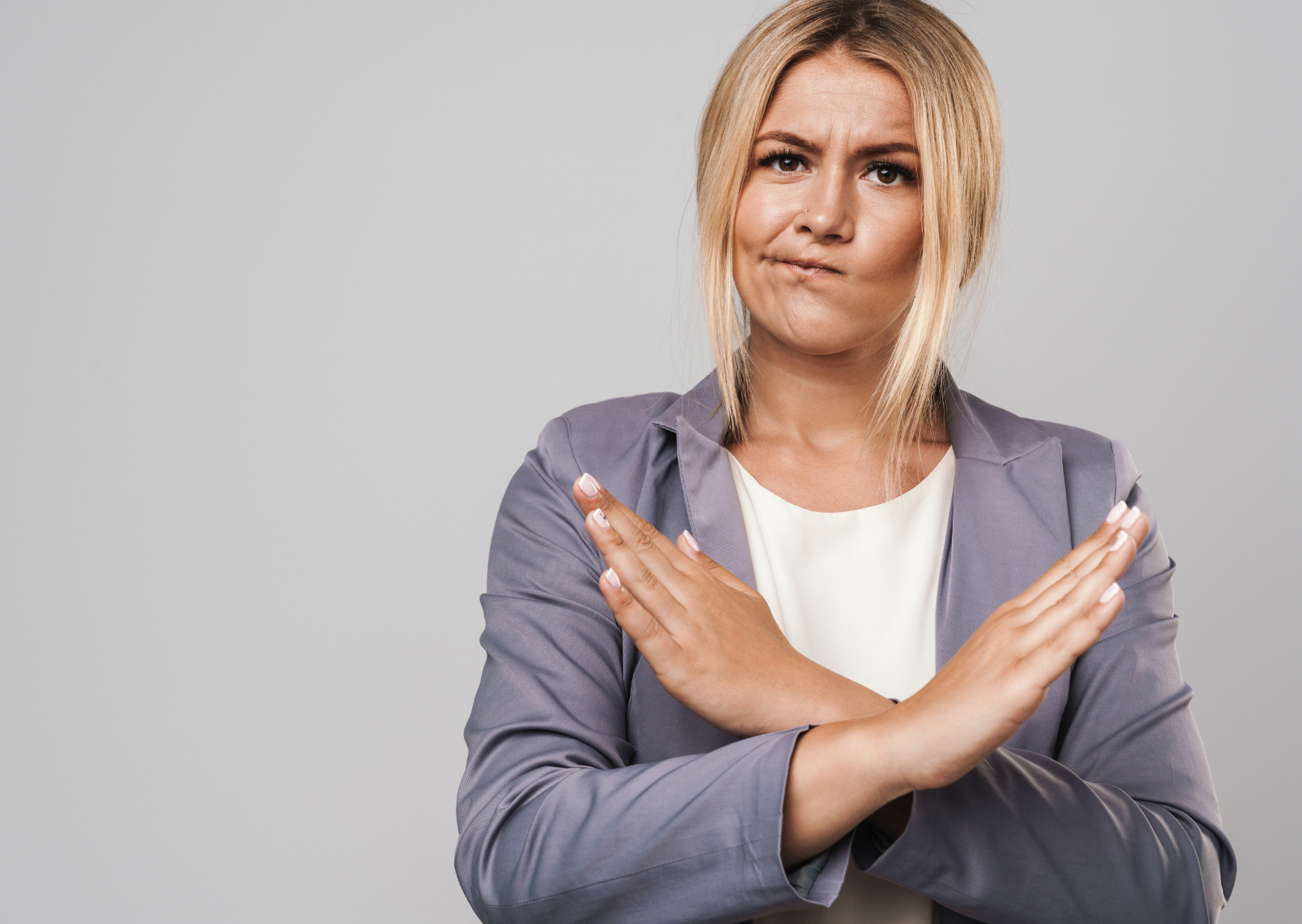 A blonde woman in a suit crossing her arms as if to say "no"