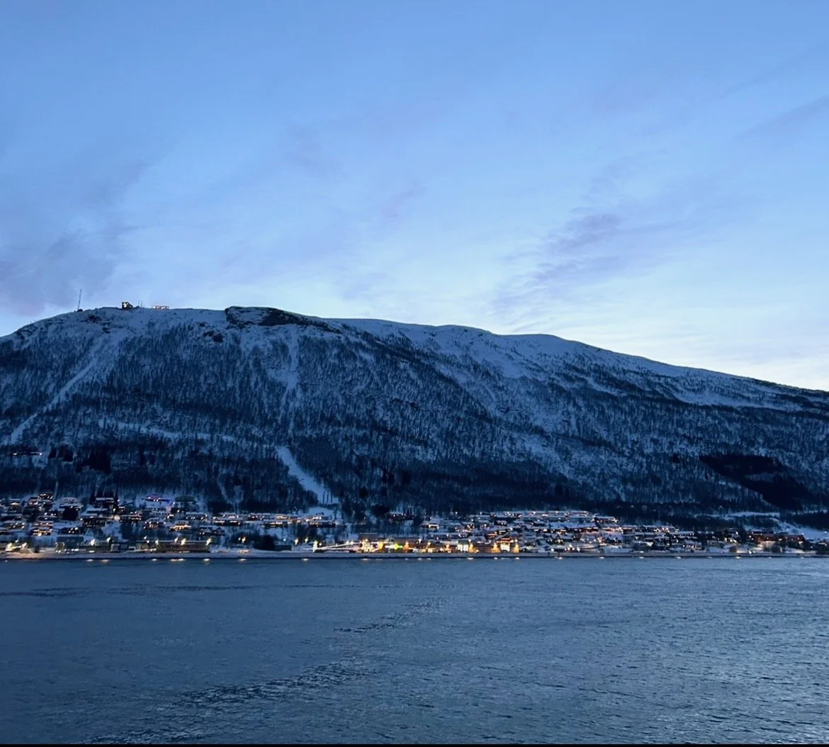 Snow-covered mountain overlooking a small town along a body of water at dusk.