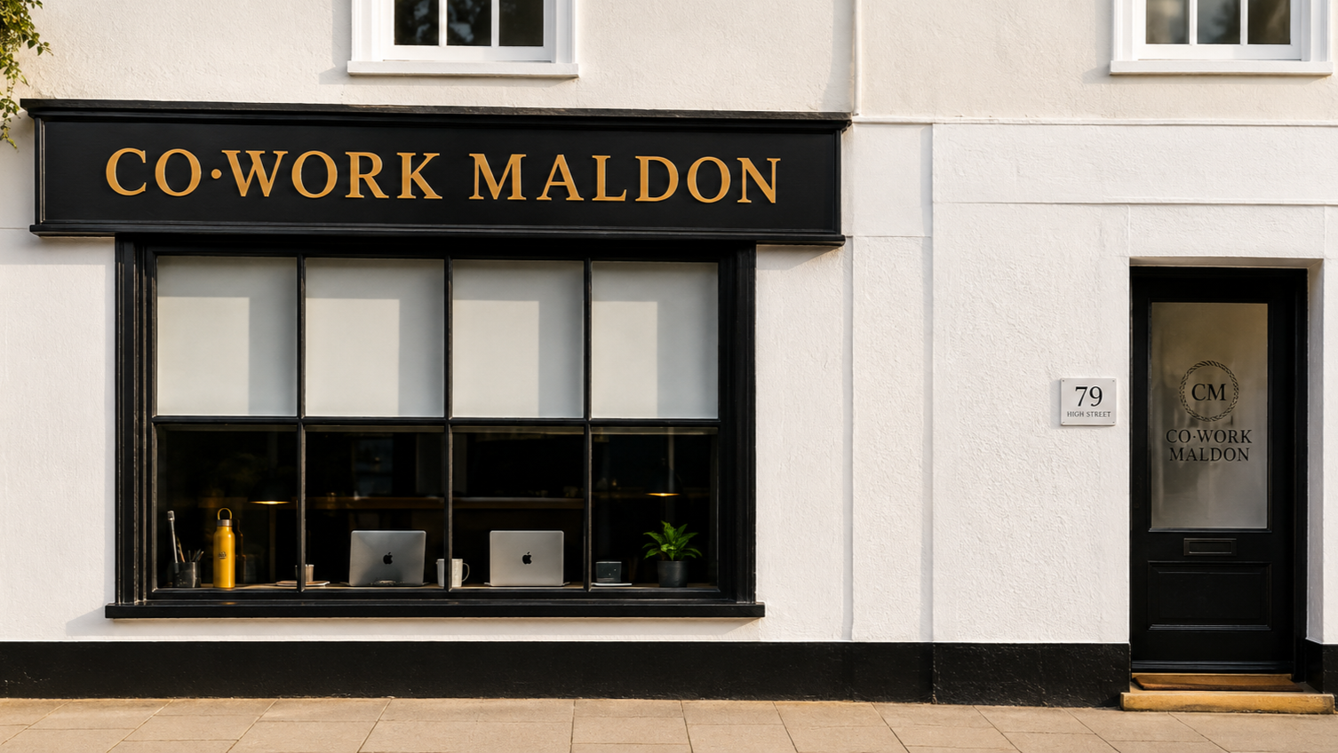 Exterior of a building with a window displaying two laptops, a water bottle, and a plant, and a sign reading 'CO·WORK MALDON' above the window. The building's address is 79 High Street.