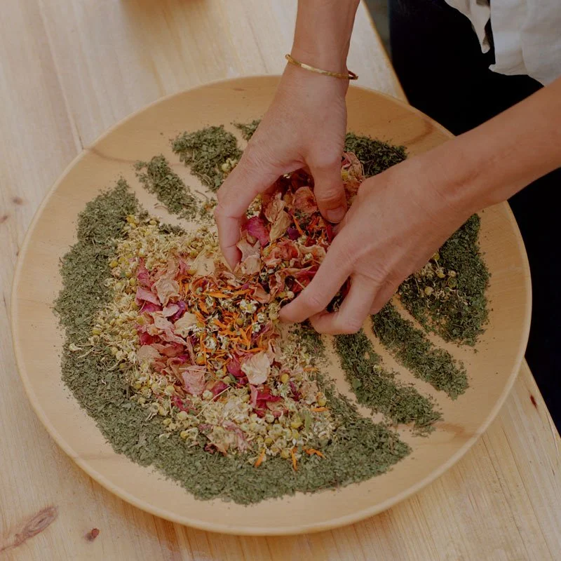 Hands mixing dried herbs and flowers on a wooden plate. Organic and biodynamic herbal tea.