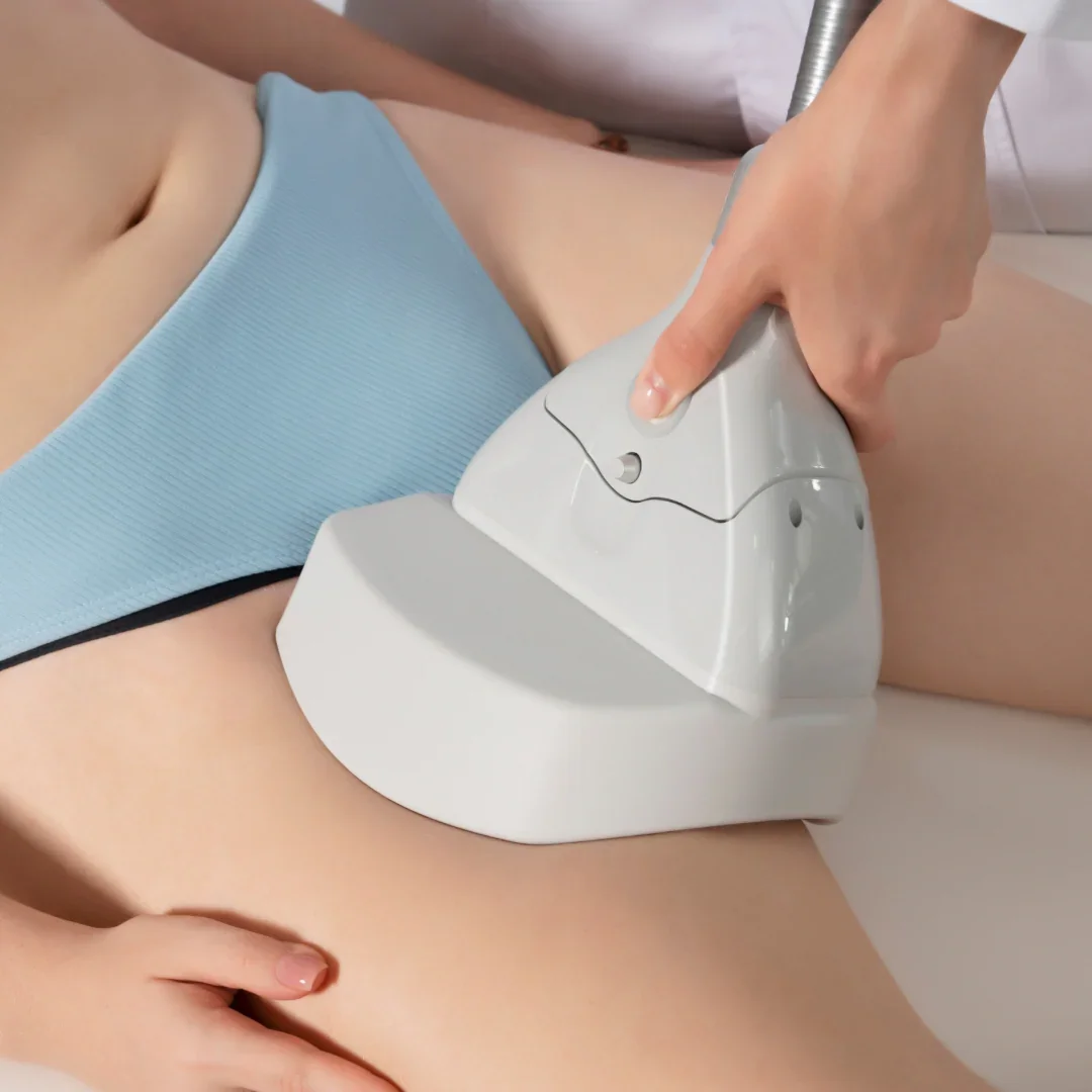 A person undergoing a medical or cosmetic procedure with a handheld device on their lower abdomen, wearing light blue shorts.