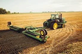 A green tractor with a mowing attachment working in a large open field.