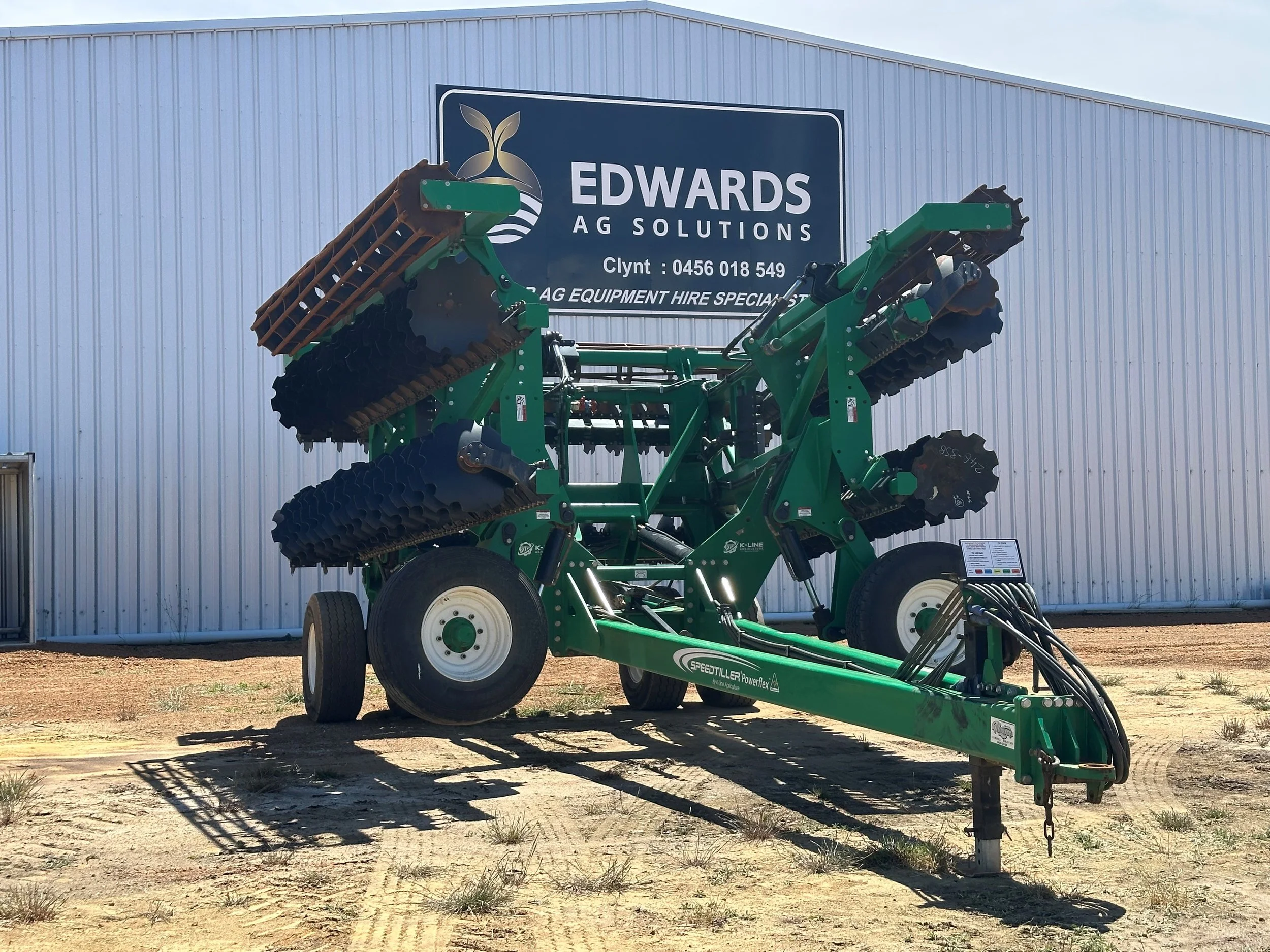 Green agricultural tillage equipment outside a building with a sign reading 'EDWARDS AG SOLUTIONS'