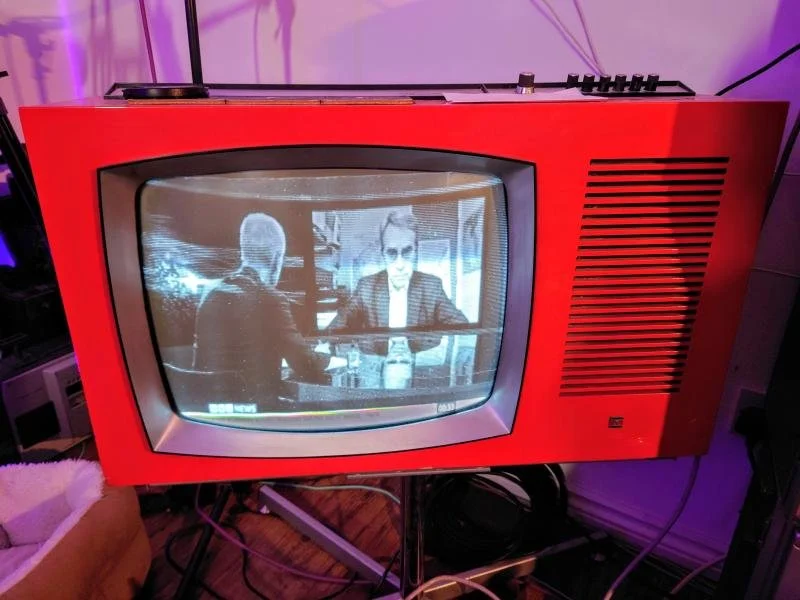 Red vintage television playing a black-and-white video of two men sitting at a table having a conversation.