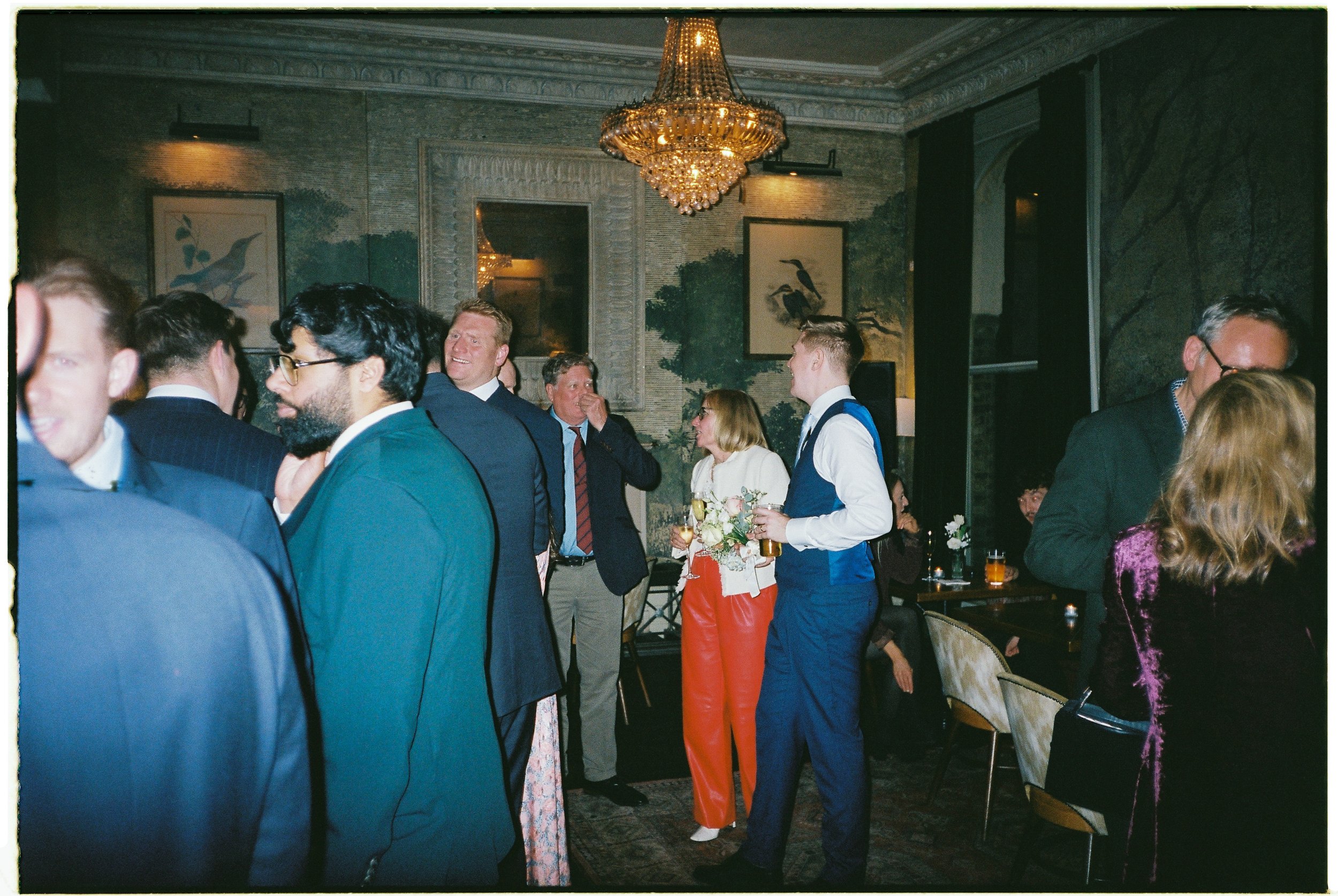 People socializing at an indoor event with elegant decor, including a chandelier and framed art on the walls.