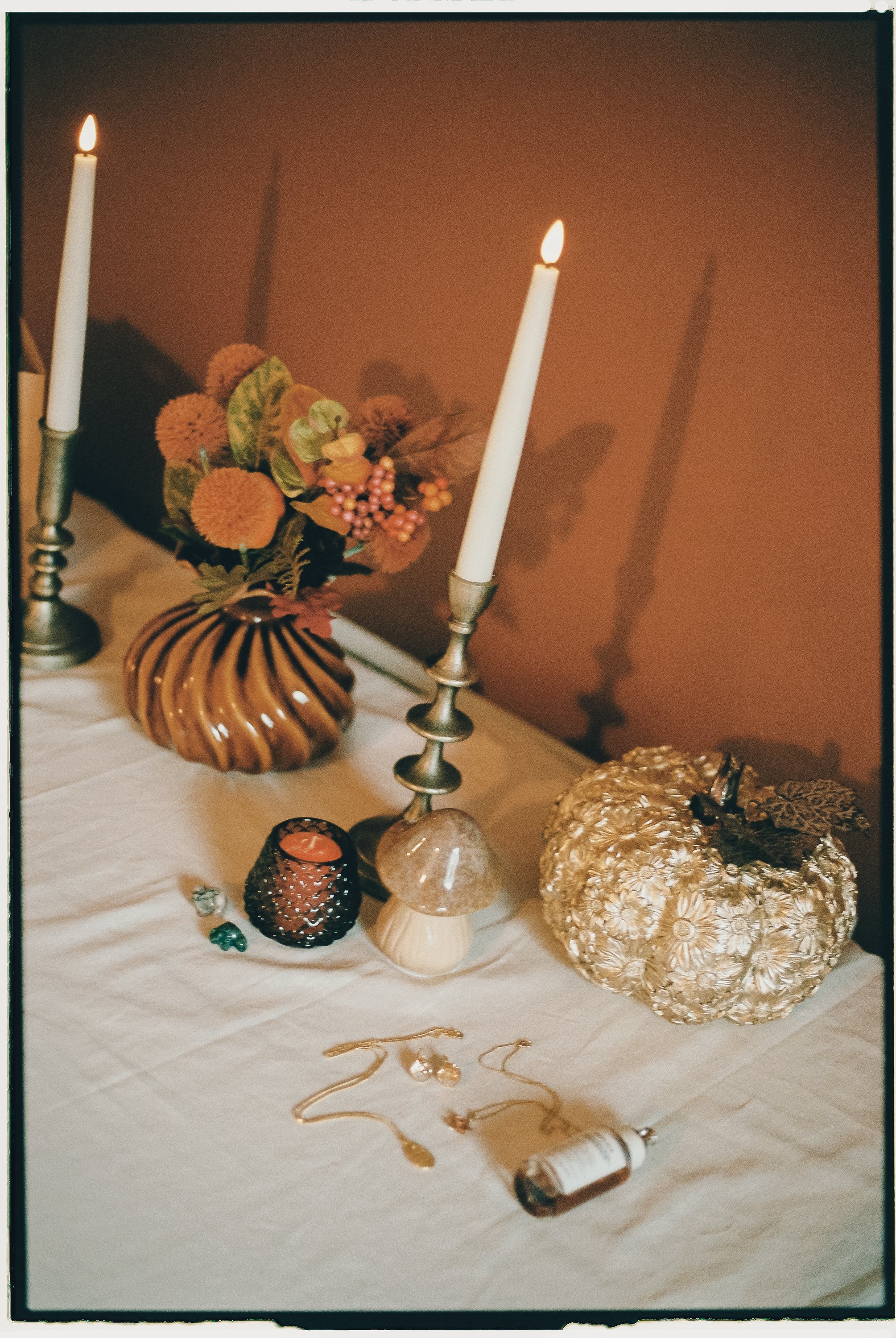 A decorated table with a floral arrangement, lit candles, jewelry, a pumpkin, and other decorative items.