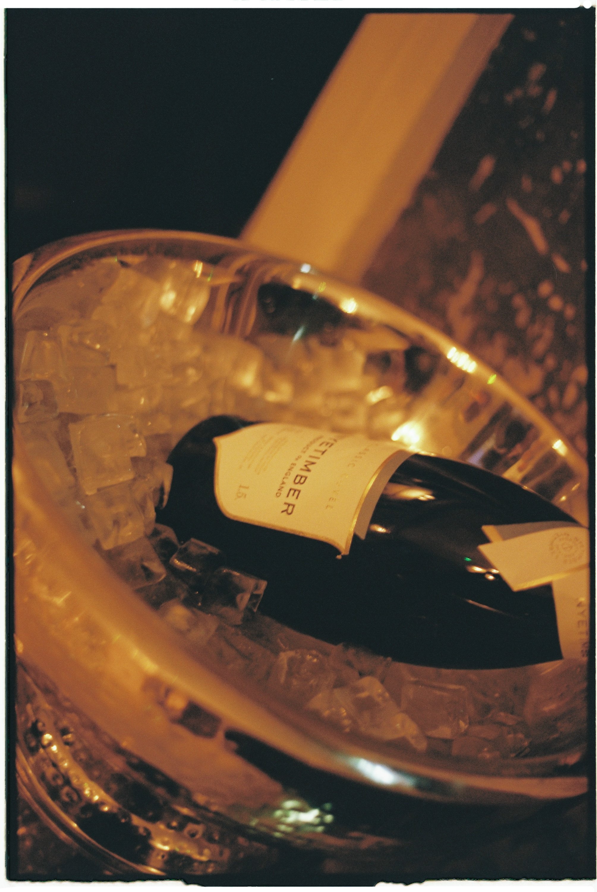 A wine bottle labeled 'Veuve Petitimer' chilling in a large glass bowl filled with ice.