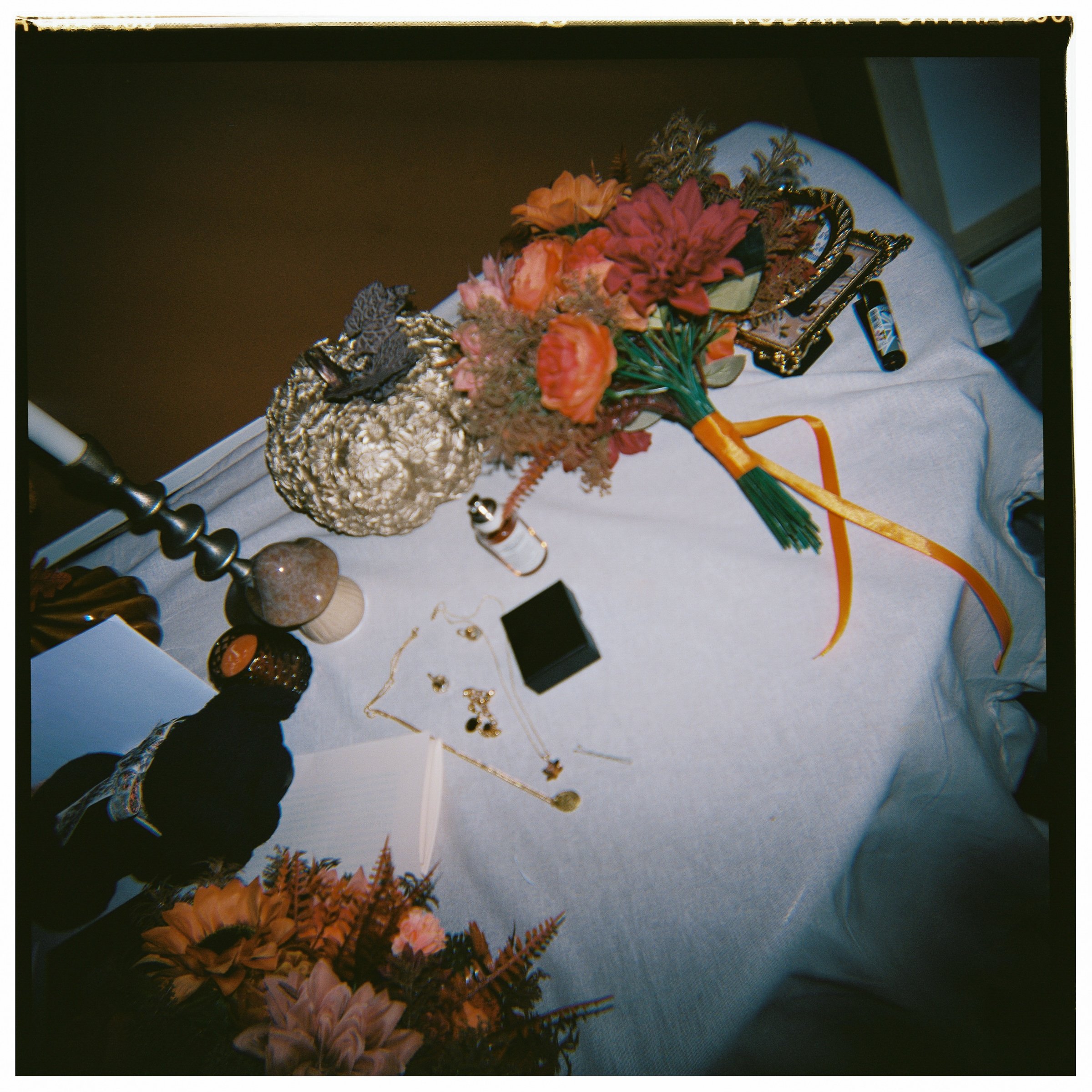 A table with a white cloth, holding a bouquet of orange and pink flowers, various jewelry, a small black box, and other decorative items.