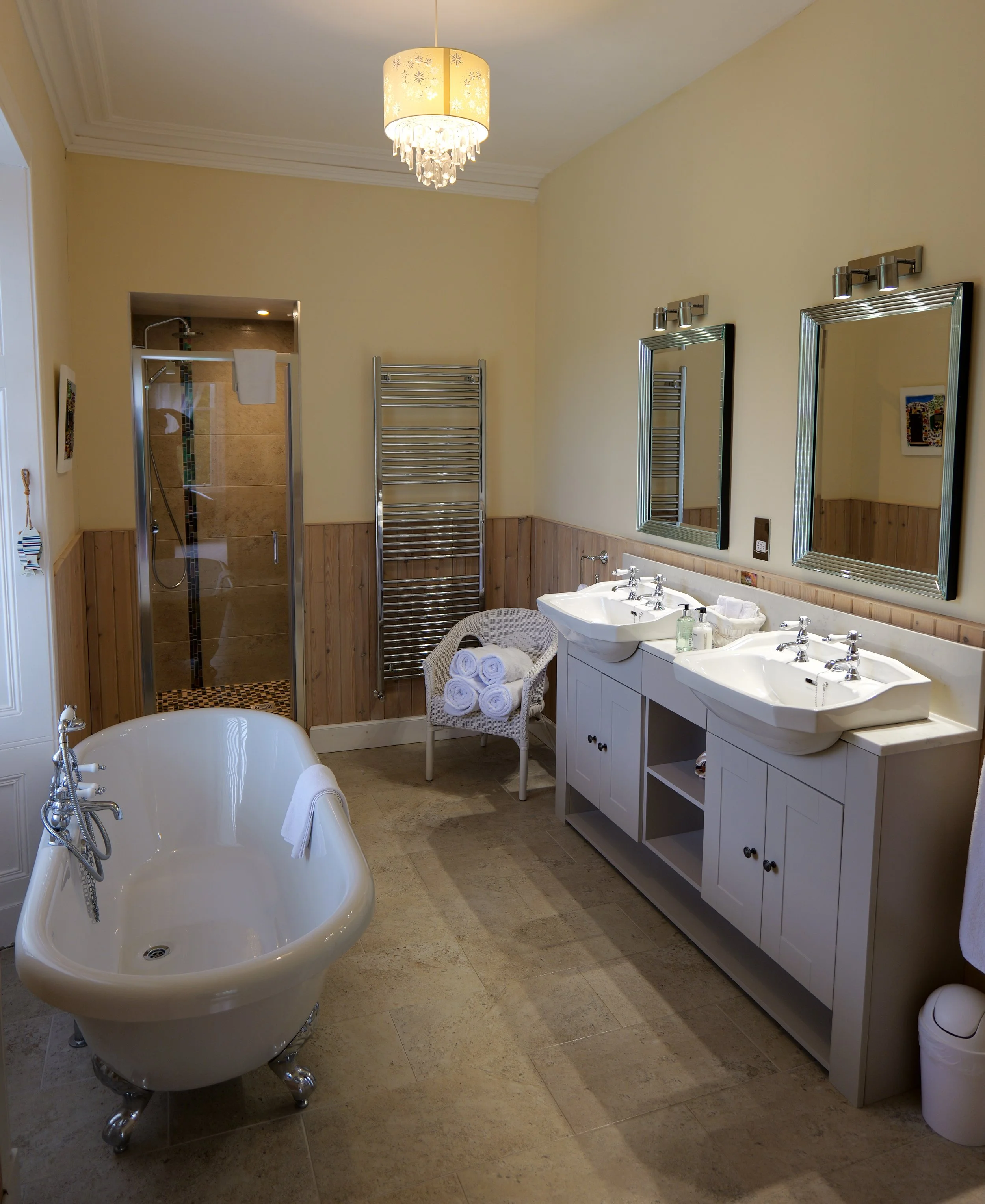 Bathroom with a clawfoot bathtub, double sink vanity, and an enclosed shower in the background.
