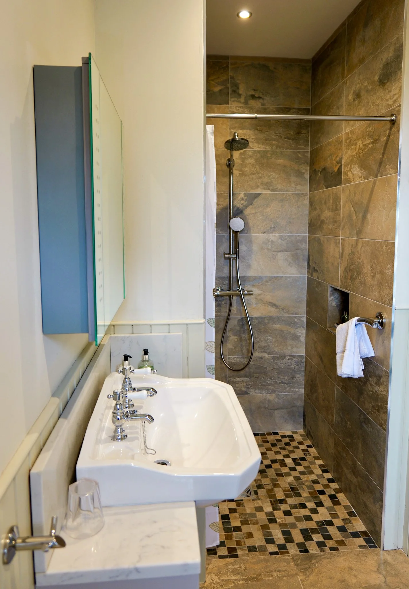 Small bathroom with a white sink, wall-mounted mirror, and a walk-in shower with brown and gray tiles.