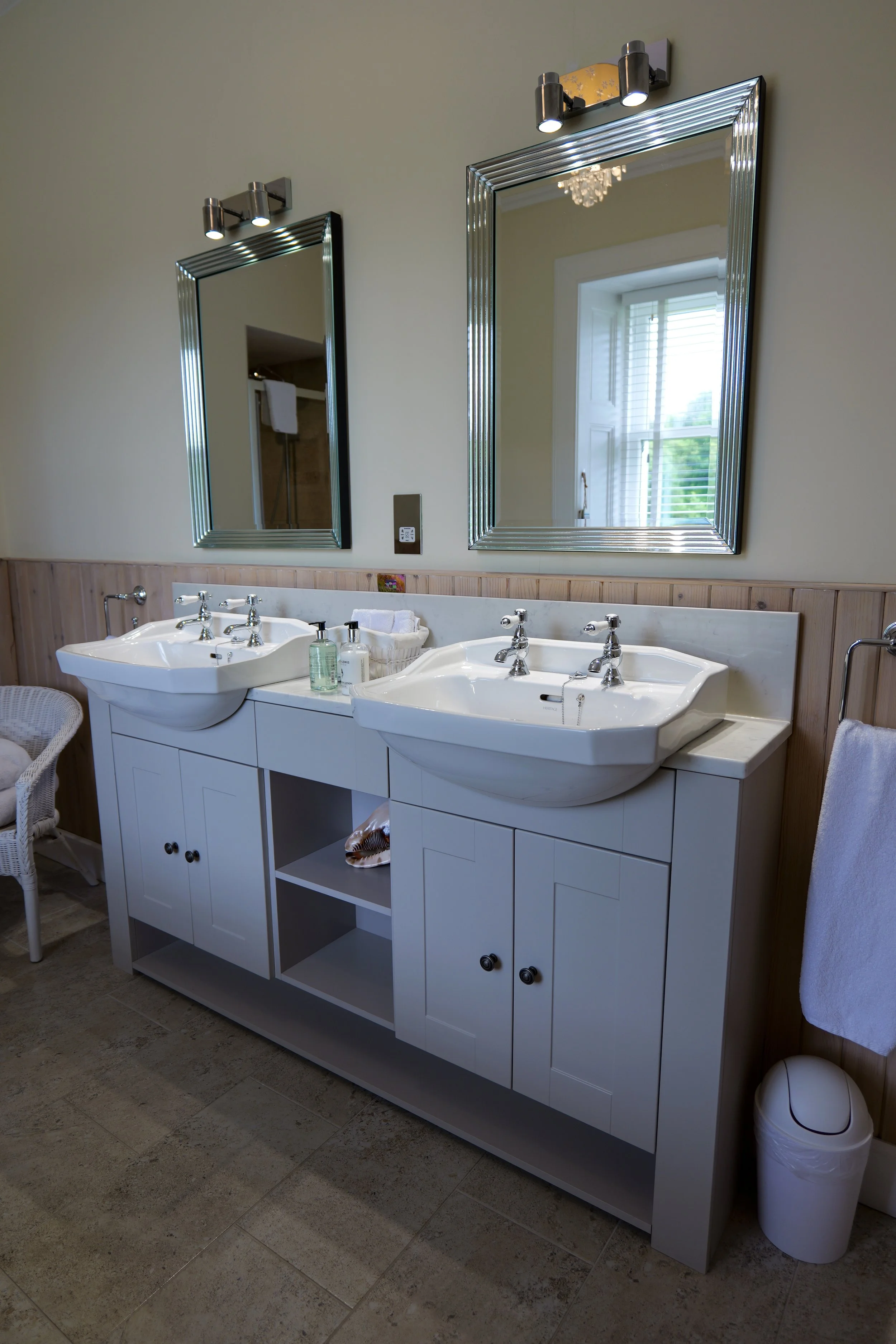 Bathroom with double vanity sinks, large mirrors, and a window with blinds.