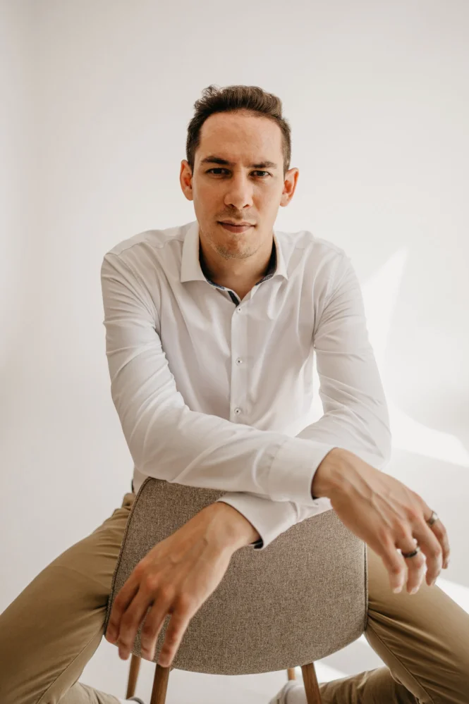 Identity coach portrait, showing a seated coach in a white shirt in a bright minimalist studio.