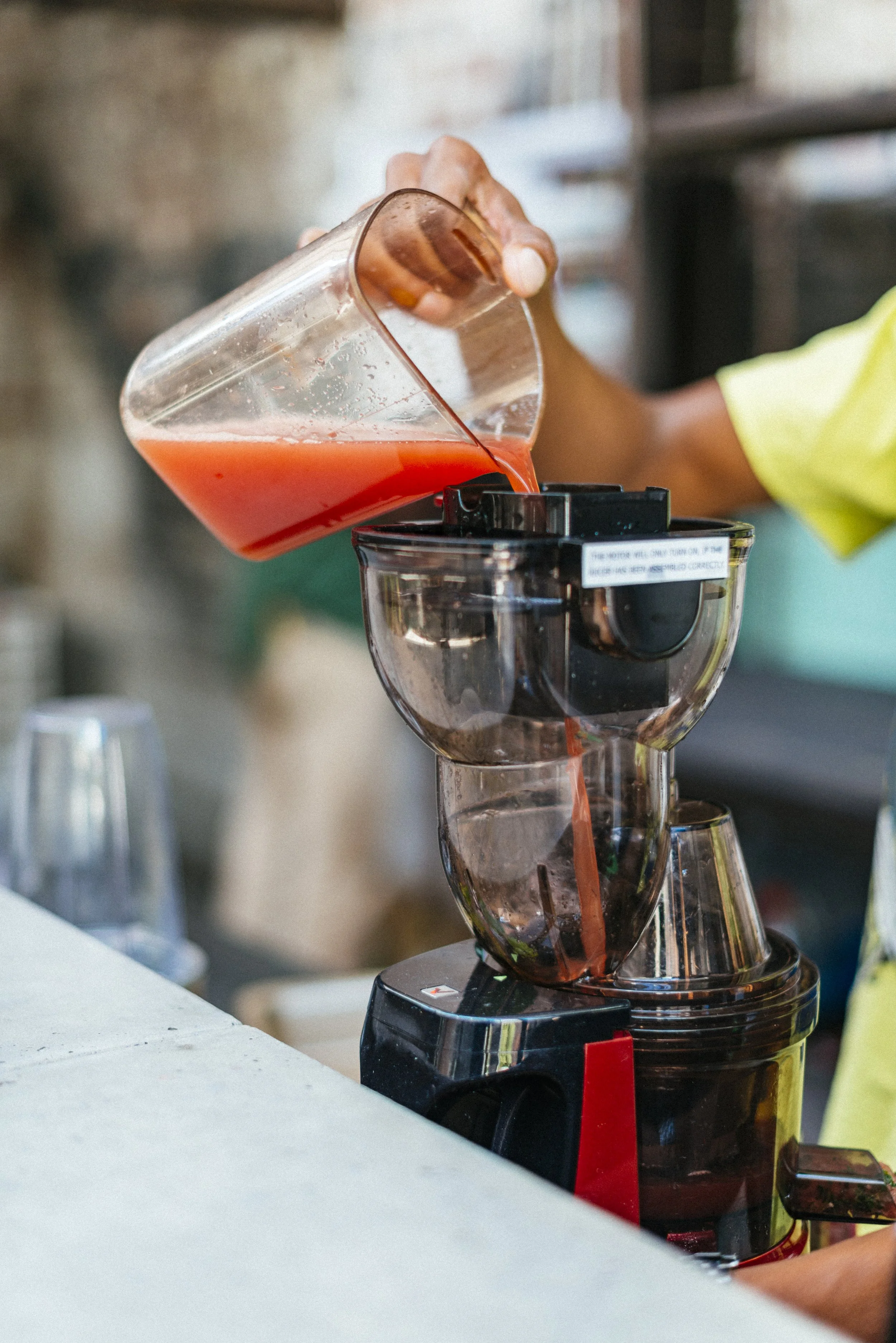 A person pouring pink liquid into a blender in a kitchen or cafe setting.