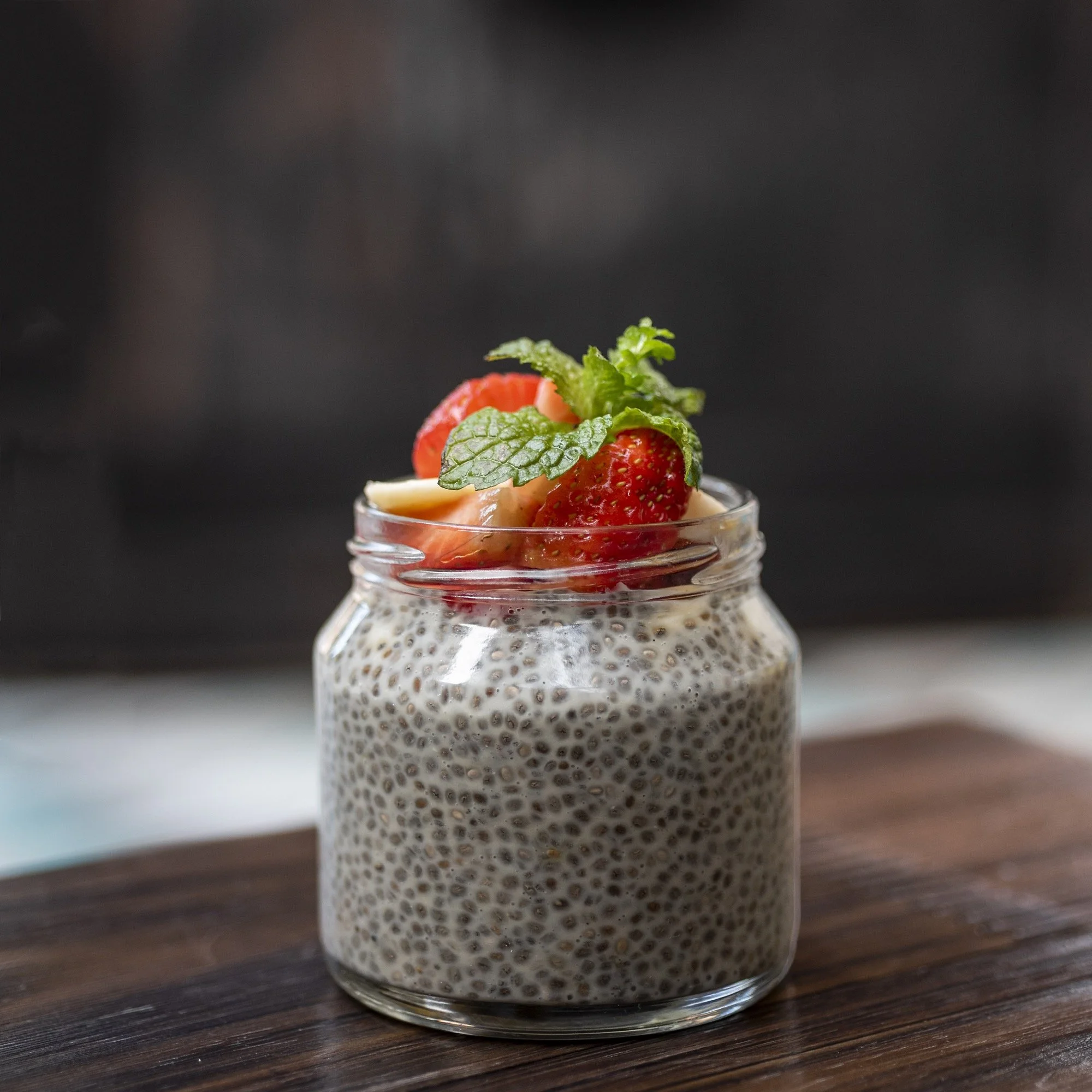Chia pudding topped with strawberries and mint leaves in a glass jar on a wooden surface.