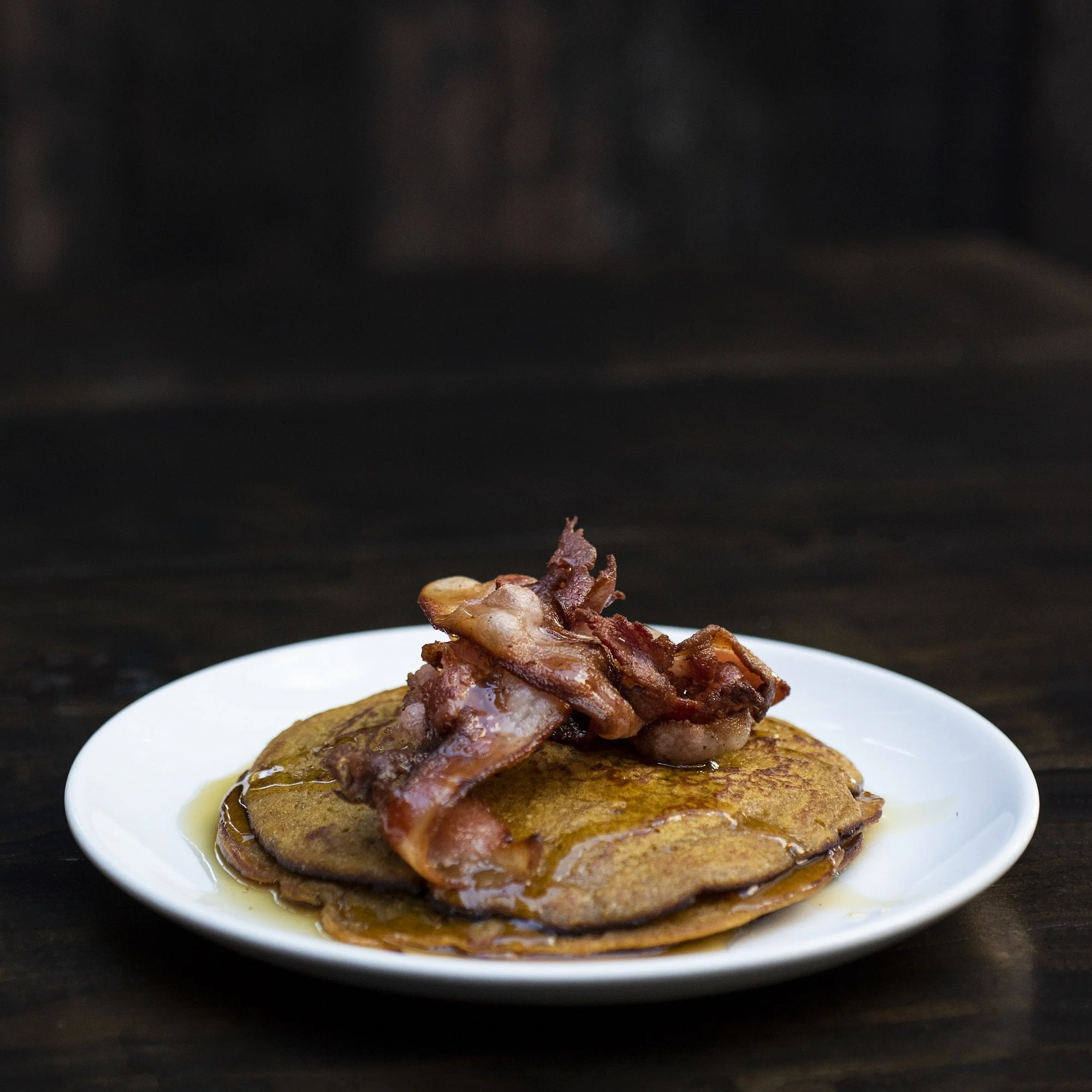 Bacon pancakes topped with bacon strips on a white plate