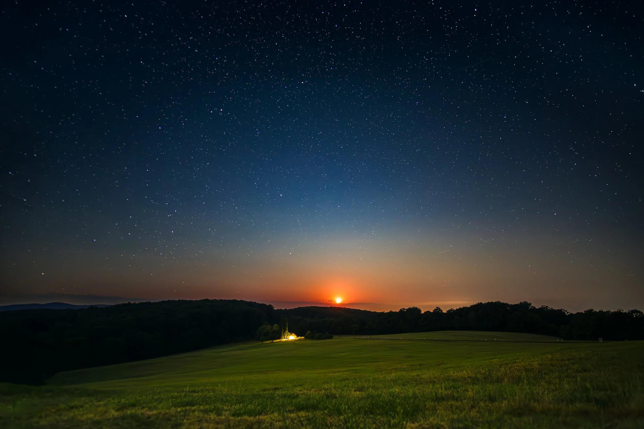 Sternenübersäter Himmel bei Sonnenuntergang über einer grünen Landschaft mit Hügeln und Bäumen.
