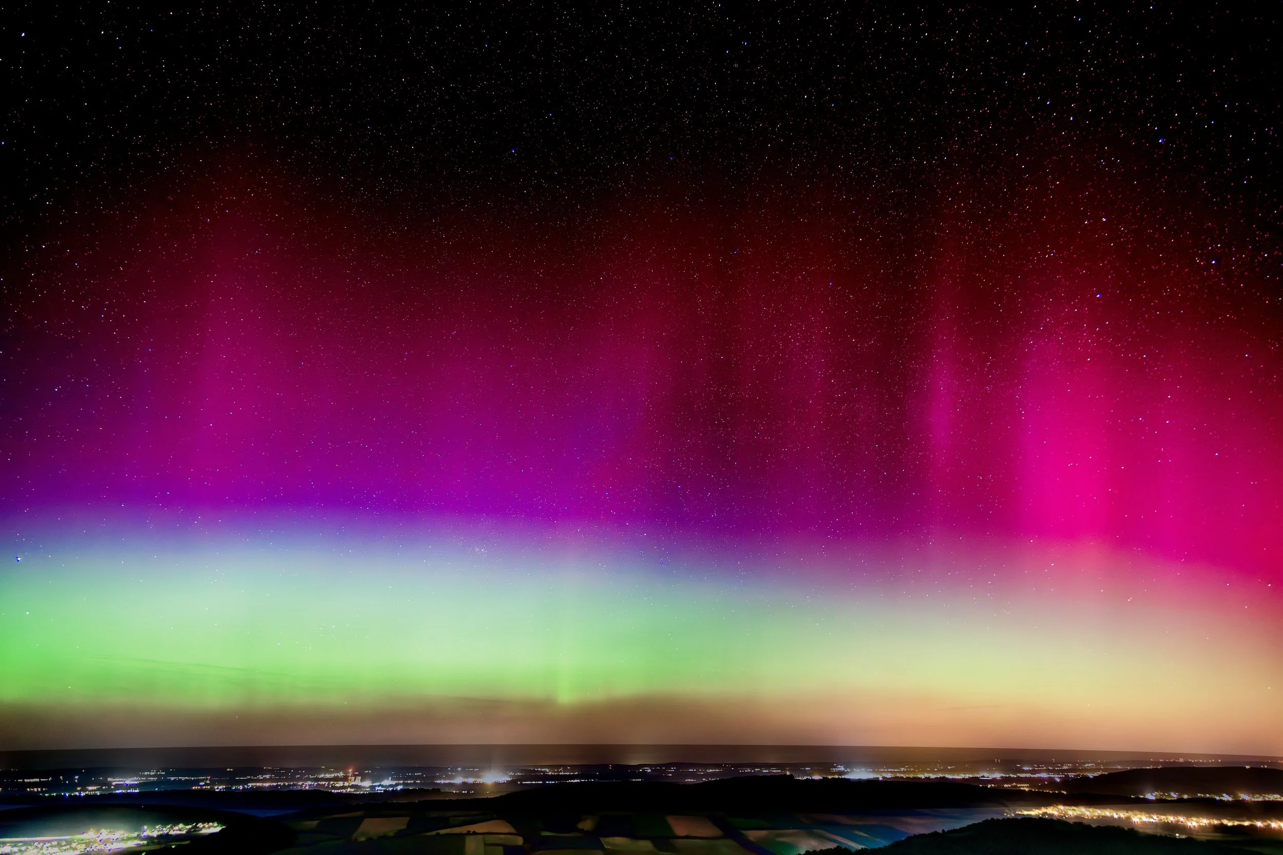 Nordlichter am Himmel über einer Landschaft bei Nacht, mit Sternen sichtbar, in Farben von Grün, Pink und Rot.