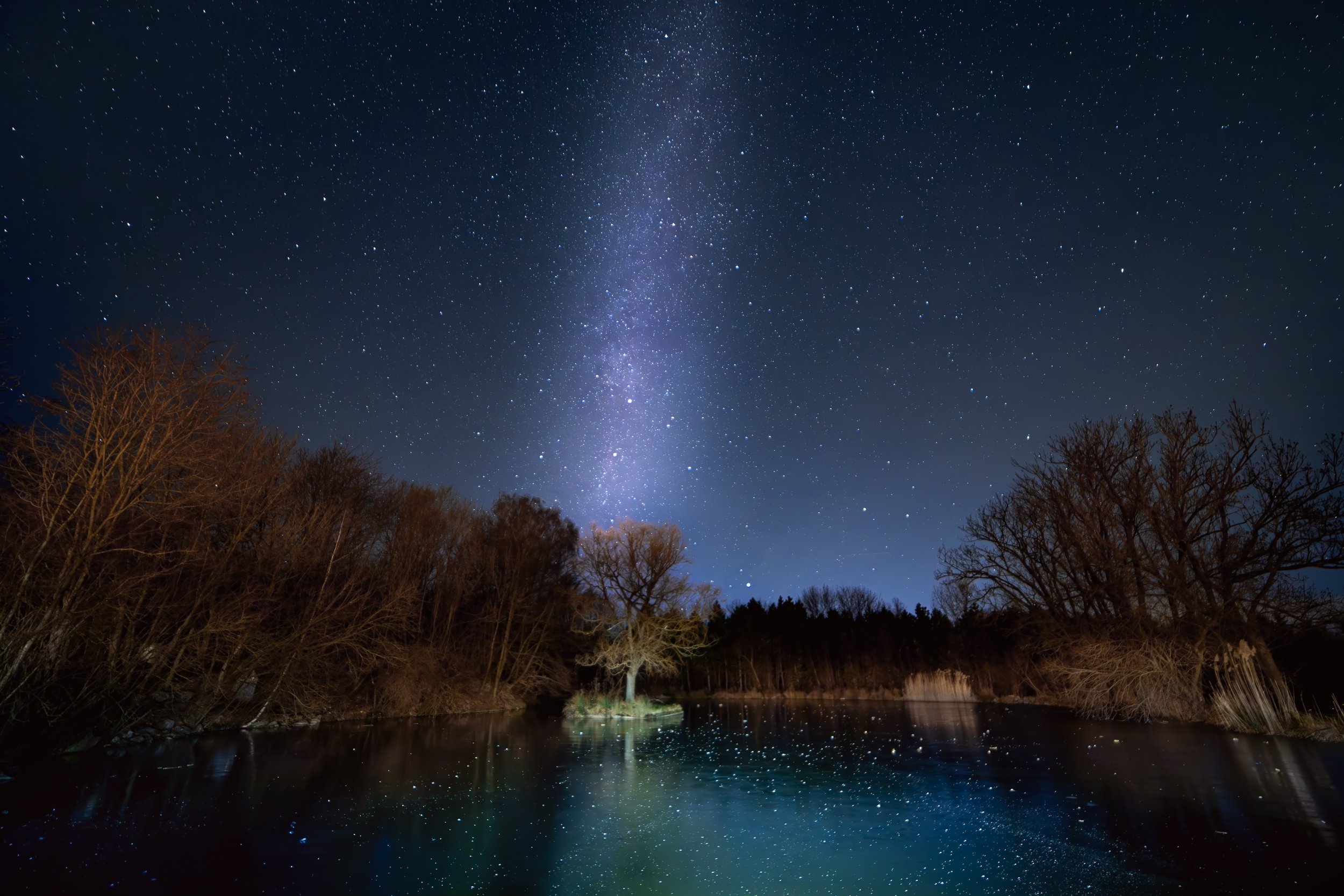 Sternenklare Nacht über einem Fluss mit Bäumen am Ufer und der Milchstraße am Himmel.