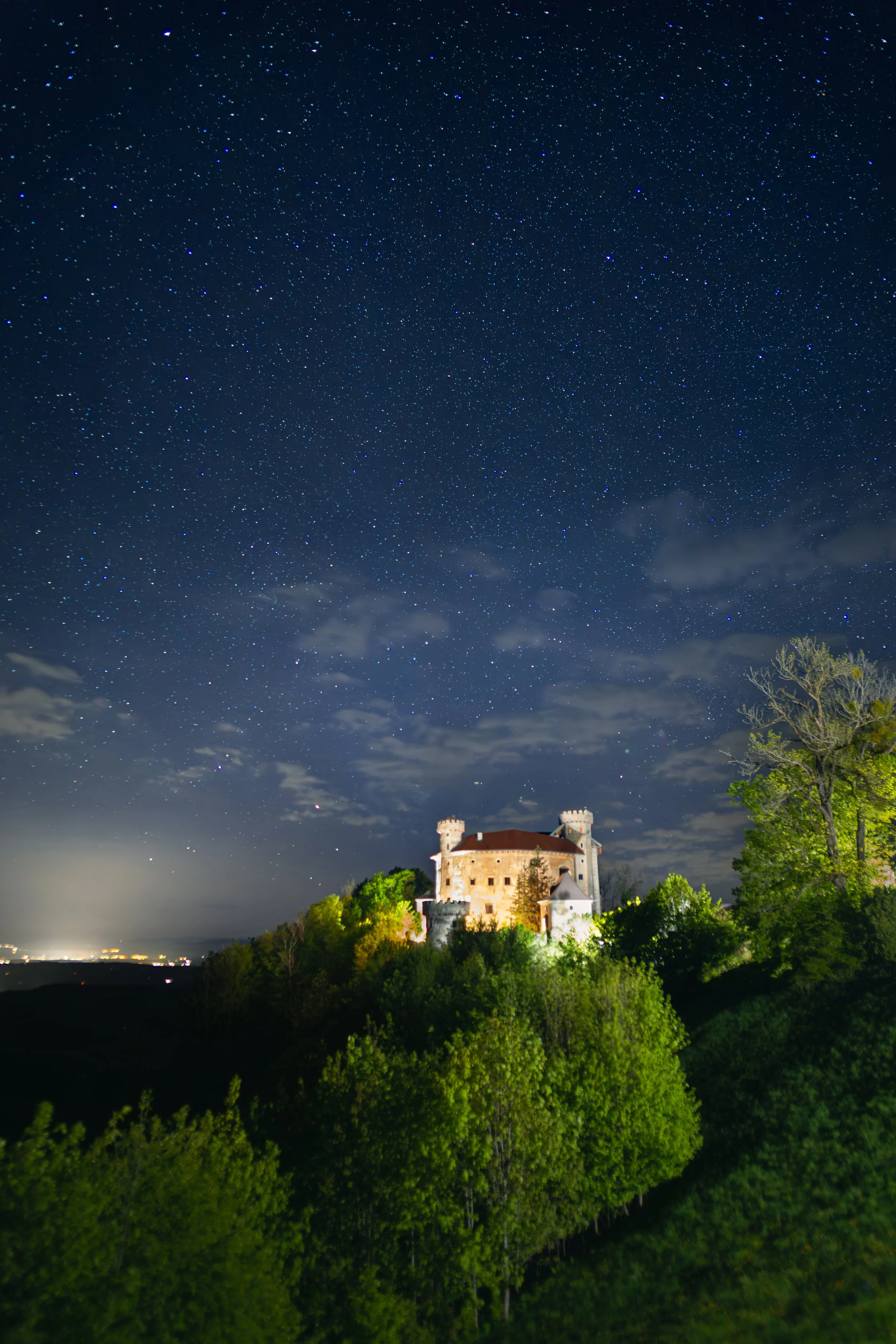 Ein beleuchtetes Schloss auf einem Hügel bei Nacht mit einem Sternenhimmel im Hintergrund.