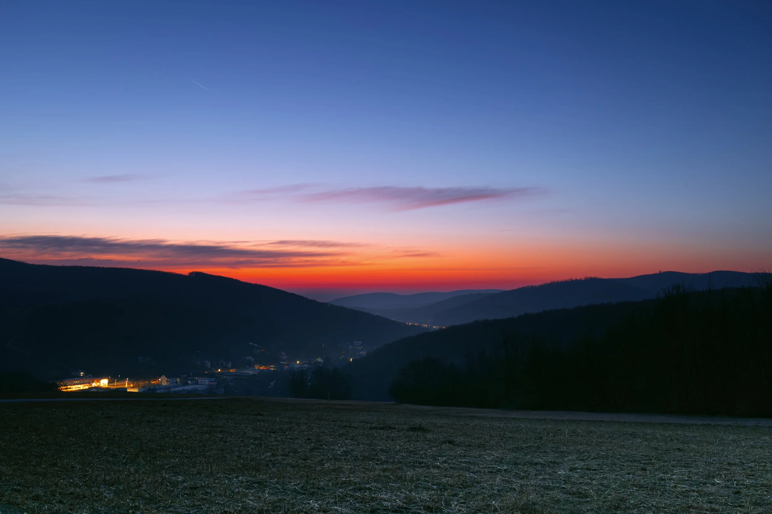 Berglandschaft bei Sonnenuntergang mit farbigem Himmel und dunklen Hügeln im Vordergrund.