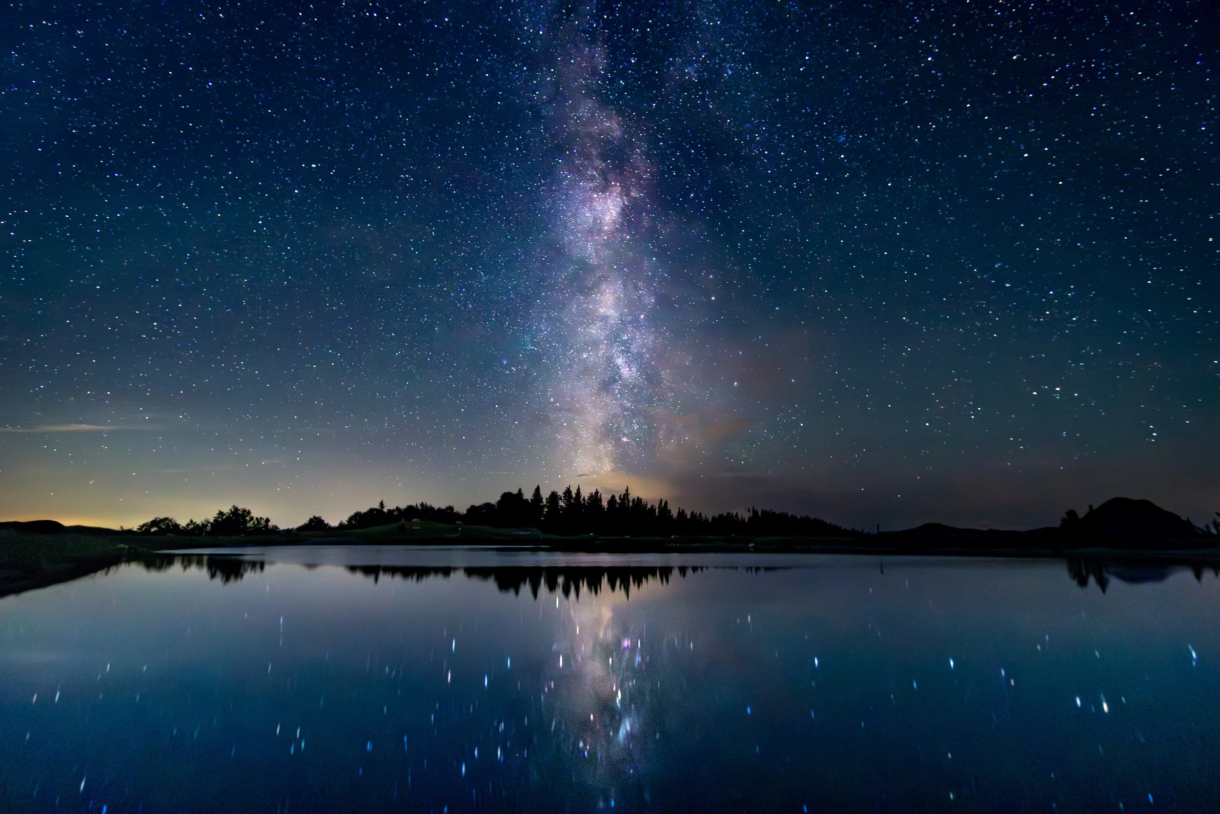 Sterne und die Milchstraße spiegeln sich in einem ruhigen See bei Nacht.