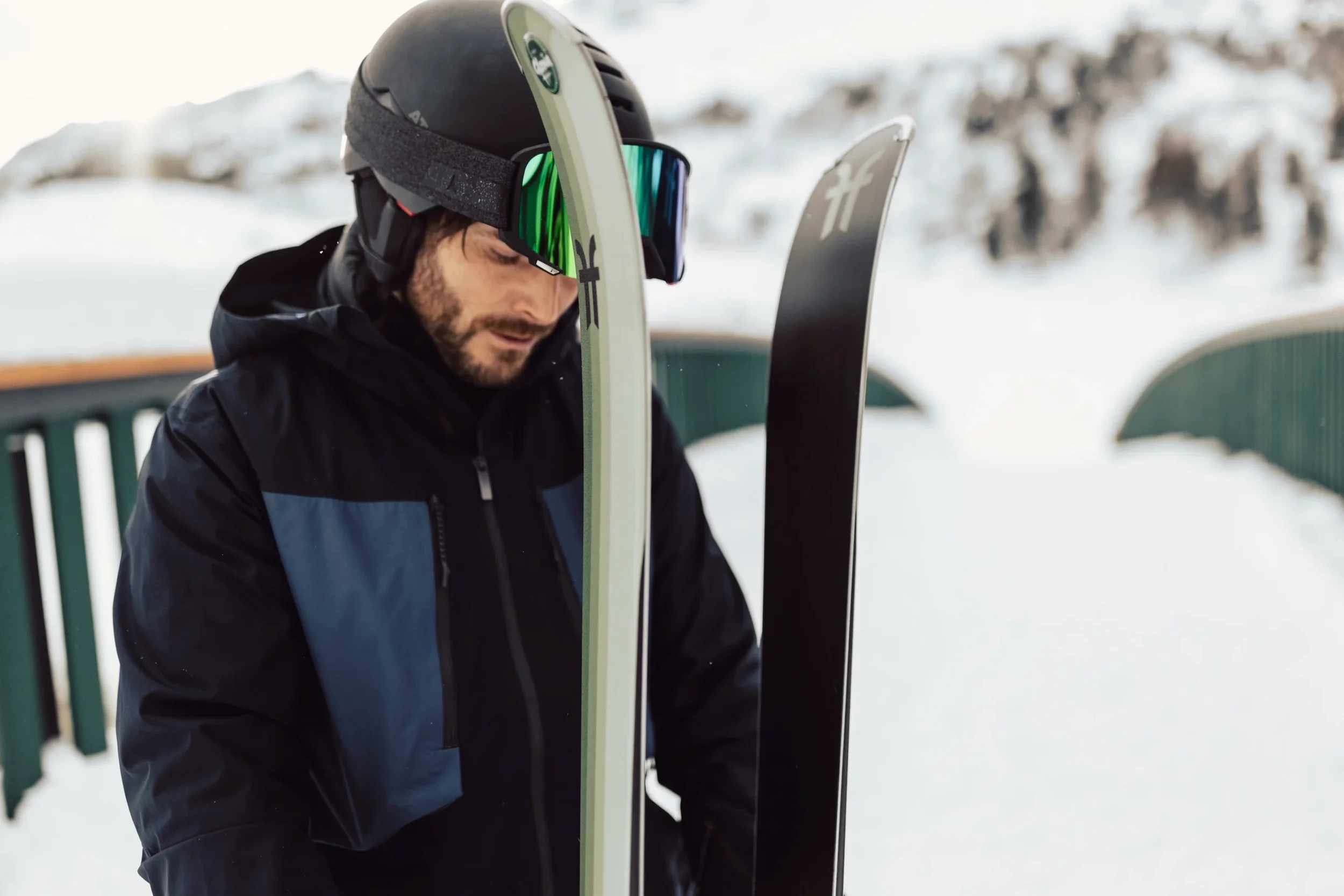 Ein Mann mit Skibrille und Helm, Skier in der Hand, im Hintergrund Schnee.
