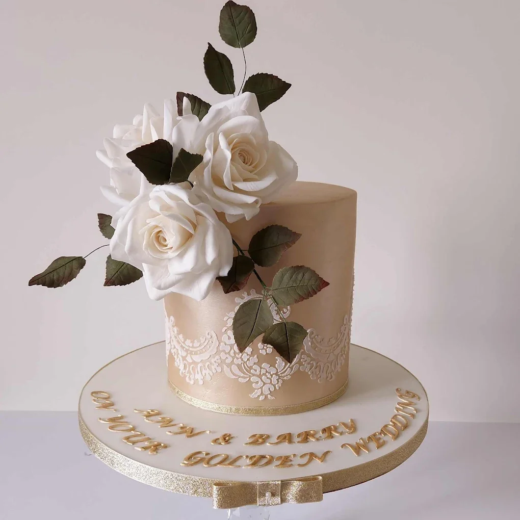 Elegant wedding cake with white roses and green leaves, beige and gold accents, and a message in gold lettering that reads "Happy Wedding to Mr. & Mrs. Golden Wedding".