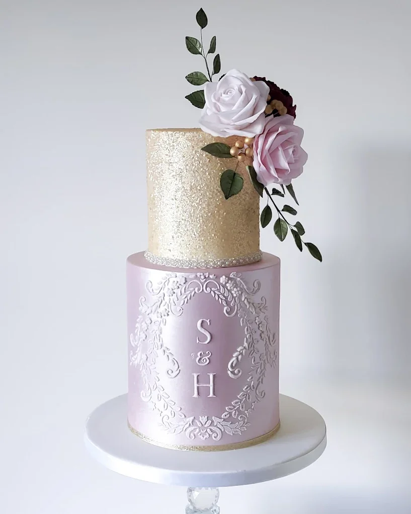 Two-tiered wedding cake with pink and gold decoration, topped with white and pink roses and greenery