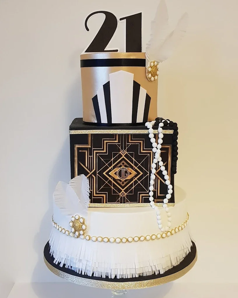 Elegant, multi-tiered cake with black, white, and gold Art Deco design, featuring pearls, feathers, and the number 21 on top, celebrating a 21st birthday.