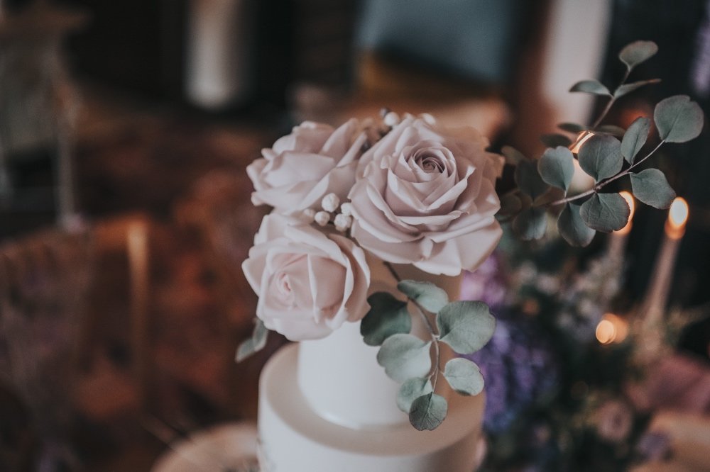 Arrangement of pale pink roses and eucalyptus leaves in a white vase on a table.