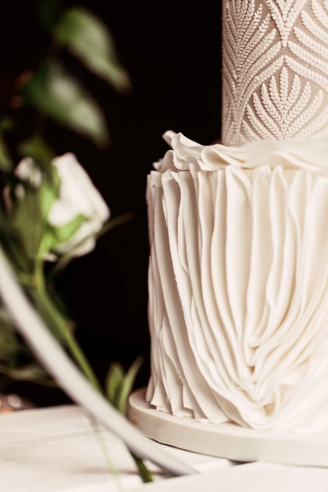 Close-up of a wedding cake with white, textured icing and floral decoration.