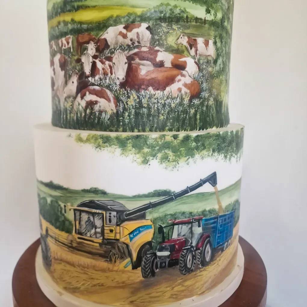 Two-tiered cake with painted farm scenes. The top tier depicts cows resting in a green field with trees in the background. The bottom tier shows a farm field with a yellow harvester and a red tractor.