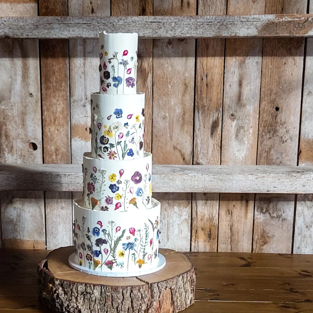 Four-tiered wedding cake with colorful floral designs placed on a wooden slab in front of a rustic wooden backdrop.