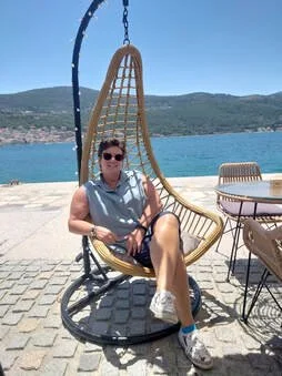 Persoon zit op een hangstoel bij het water, met bergen op de achtergrond.