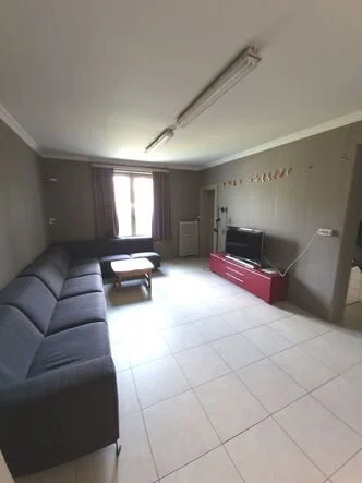 Een woonkamer met een grote L-vormige bank, een tv op een rode tv-meubel, een raam met gordijnen, en een salontafel.