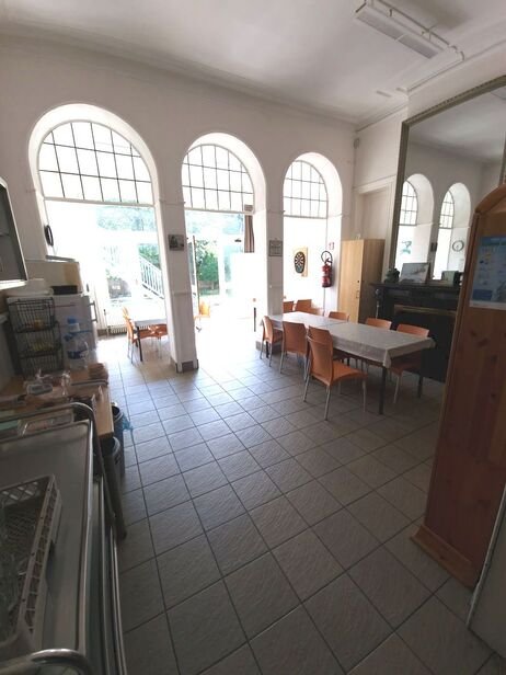 Binnenruimte met grote, gebogen ramen, tafels en stoelen, en een keukenunit.