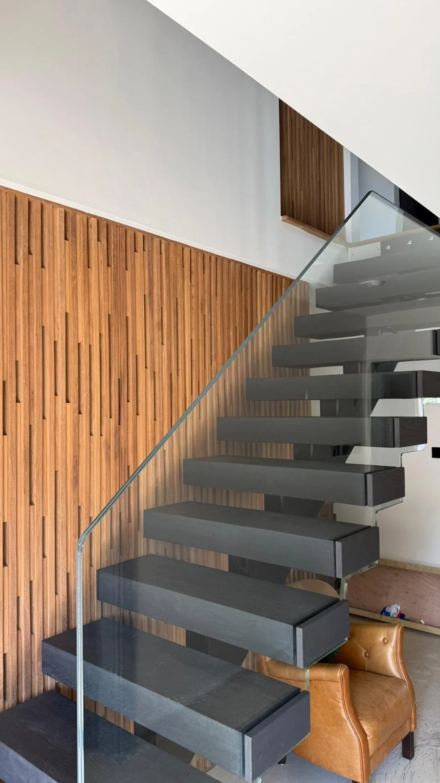 Modern staircase with dark wooden steps, glass railing, and a wooden accent wall in a contemporary interior.
