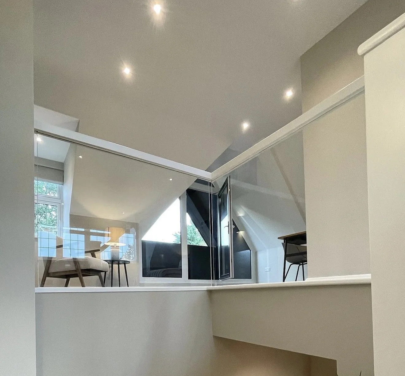 Modern living space with sloped ceiling, large window, and a seating area with chairs and a table, viewed from below.
