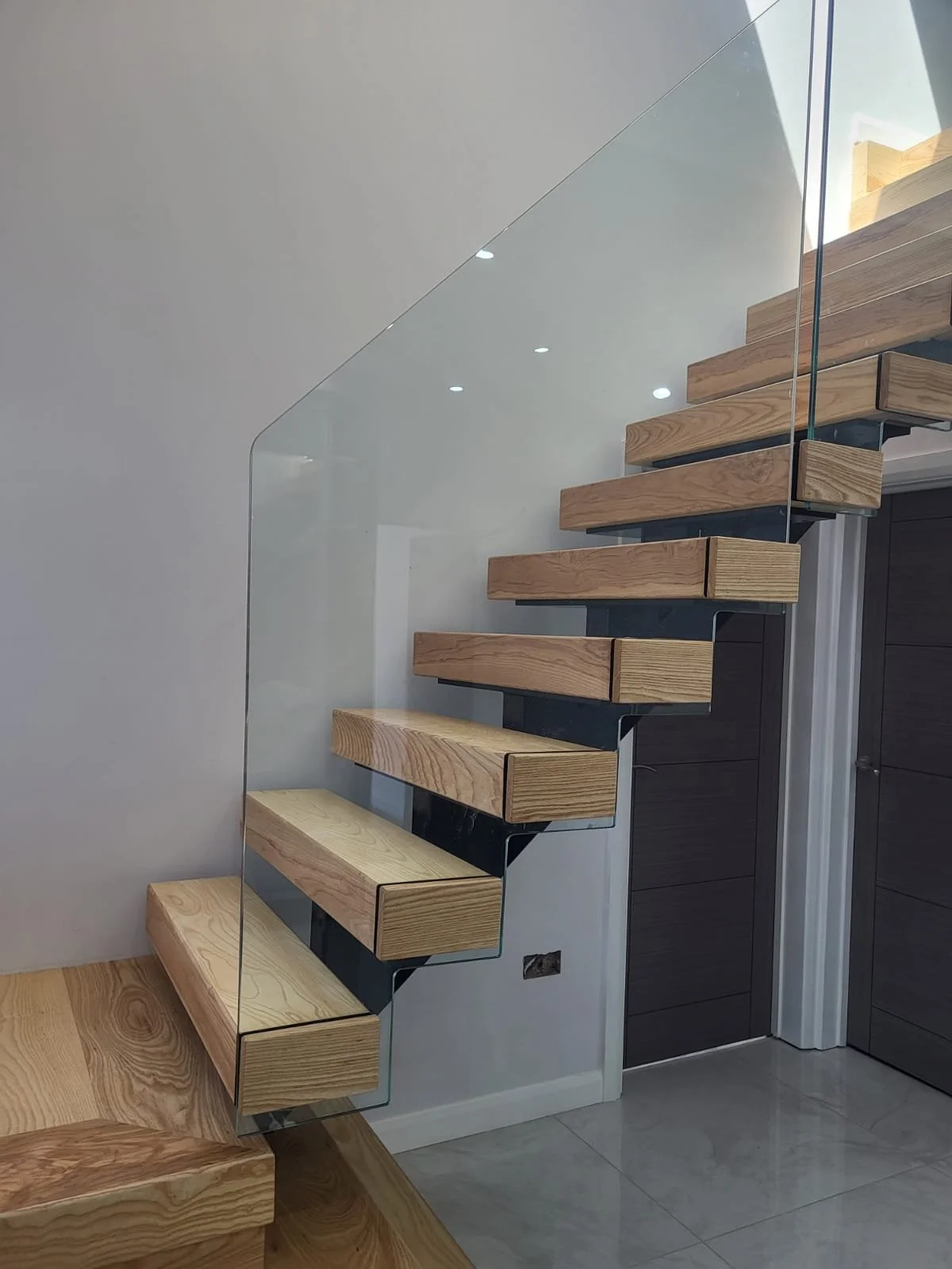 Modern floating wooden staircase with glass railing in interior space.