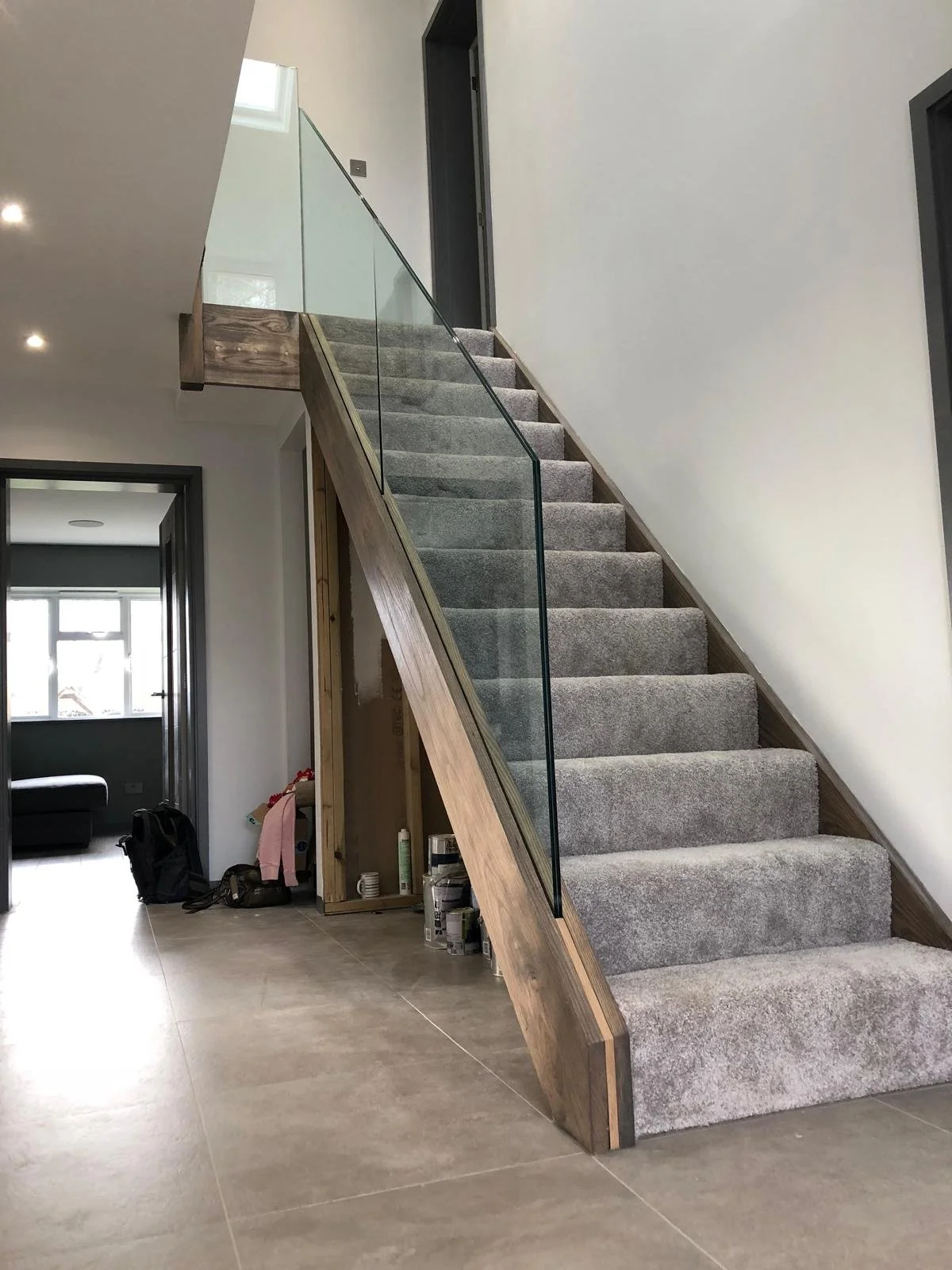Empty staircase with grey carpet, glass railing, wooden frame, leading to upper floor in a modern house interior.