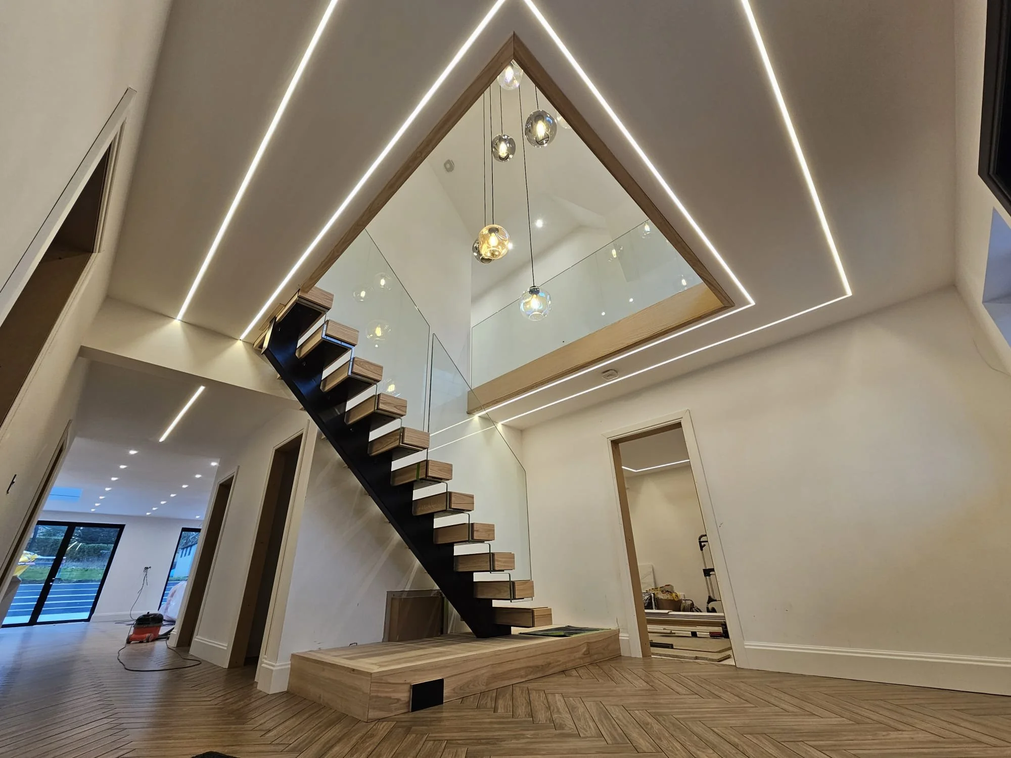 Modern interior with wooden staircase, mirrored ceiling, and LED strip lighting in a spacious room.