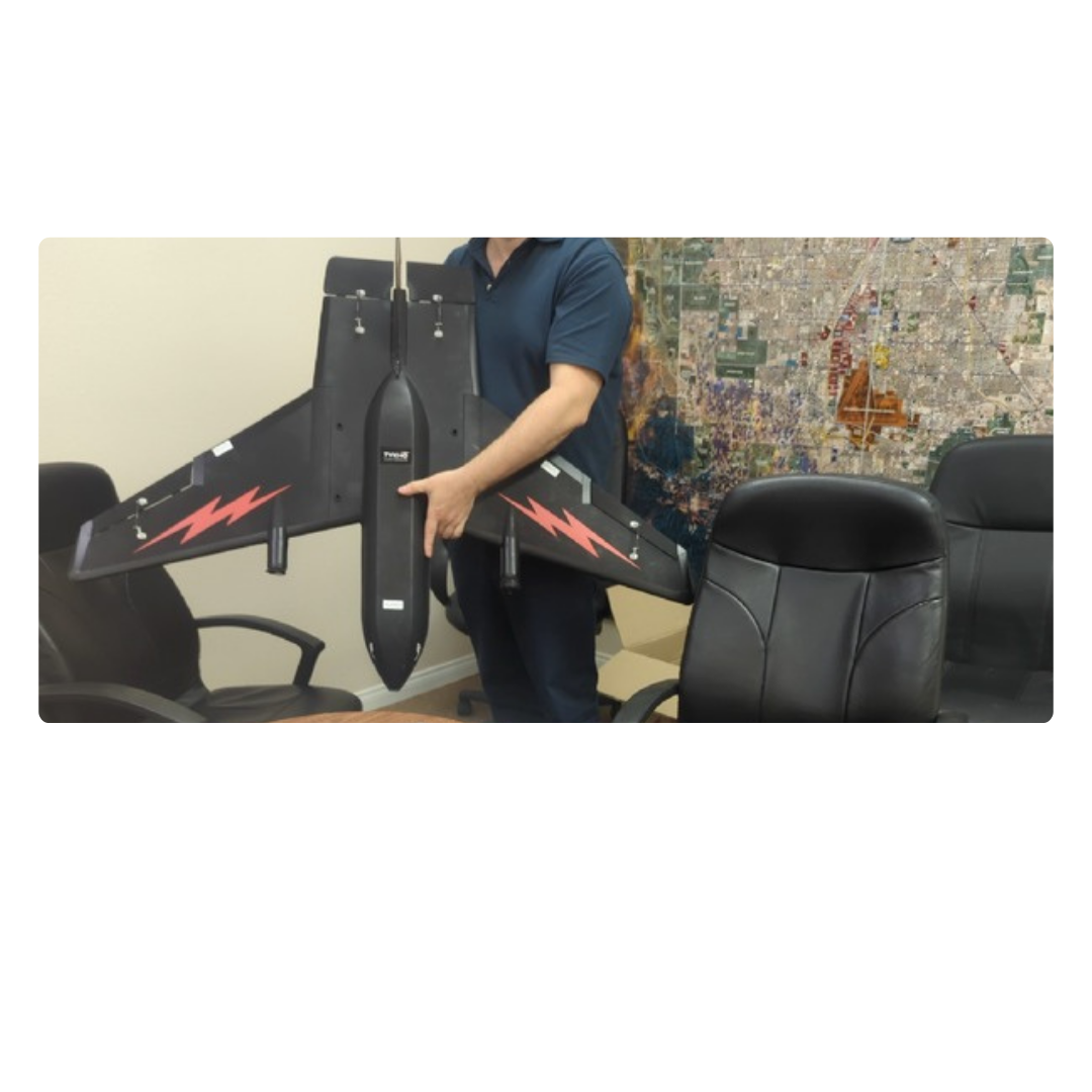 Person holding a large black drone with red lightning bolt decals in a conference room with chairs and a city map on the wall.