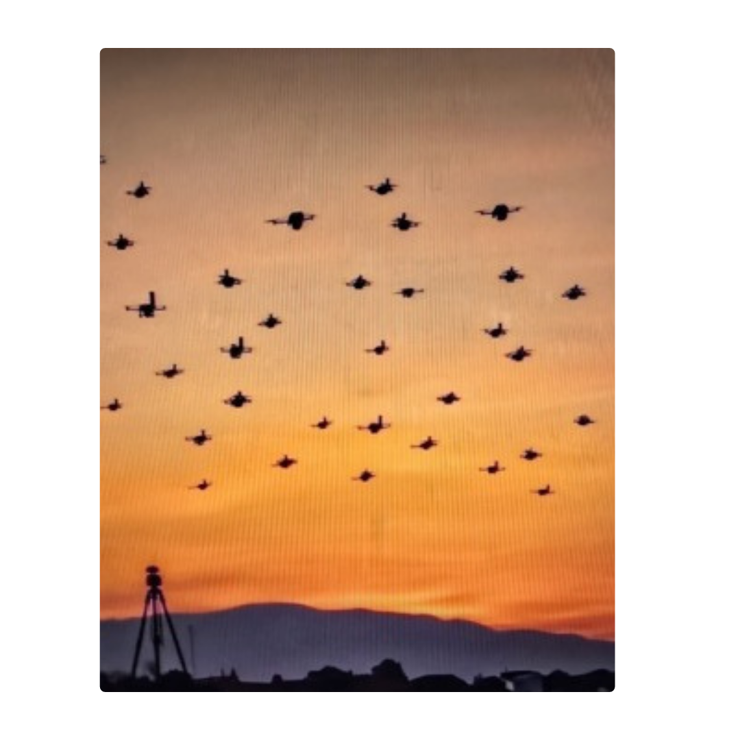 A formation of fighter jets flying in a V-shape pattern during sunset with mountains below and a camera mounted on a tripod in the foreground.
