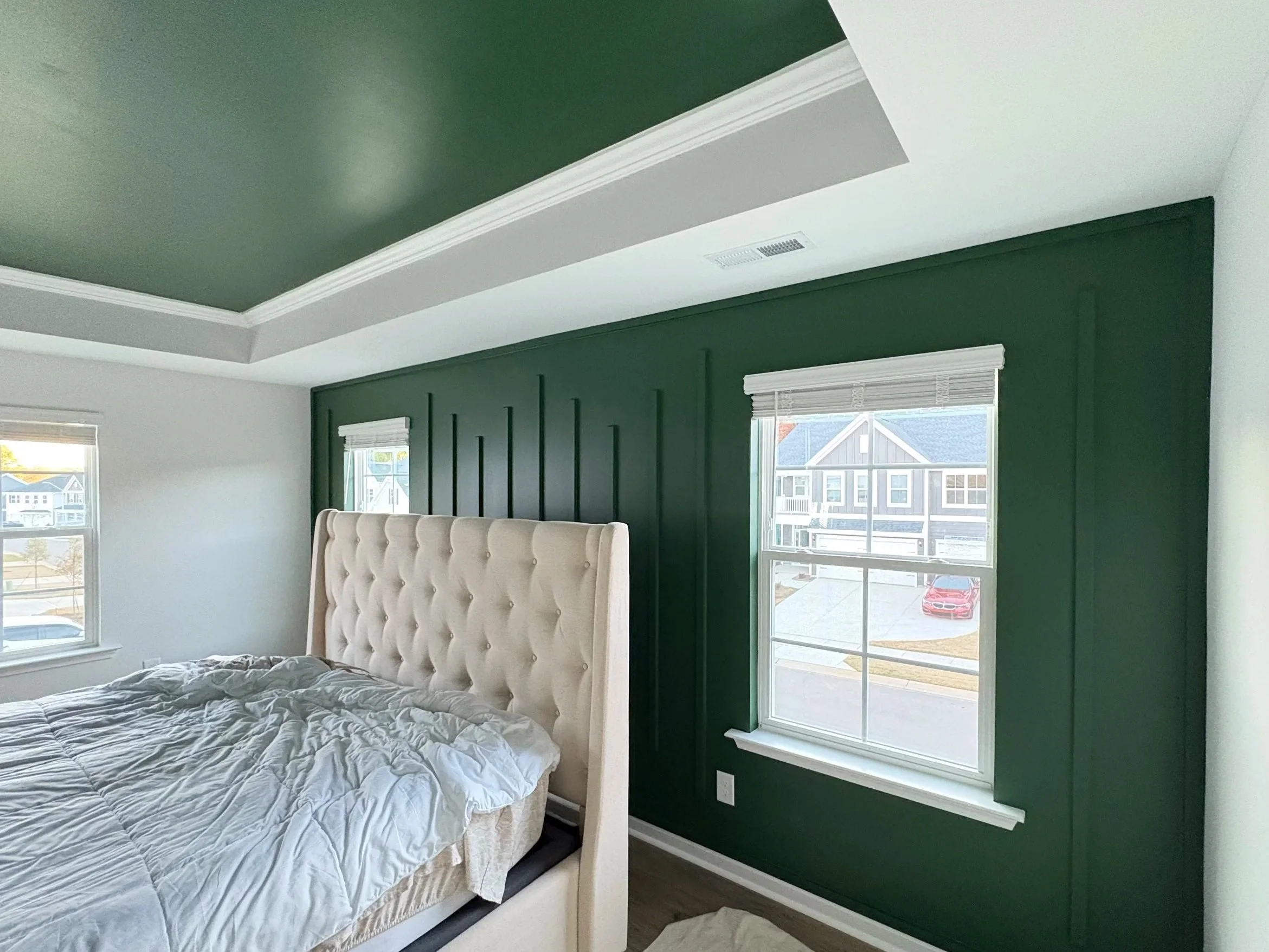 Bedroom featuring a green accent wall and matching green tray ceiling with custom trim work by Cardinal Custom Finishes in Holly Springs NC